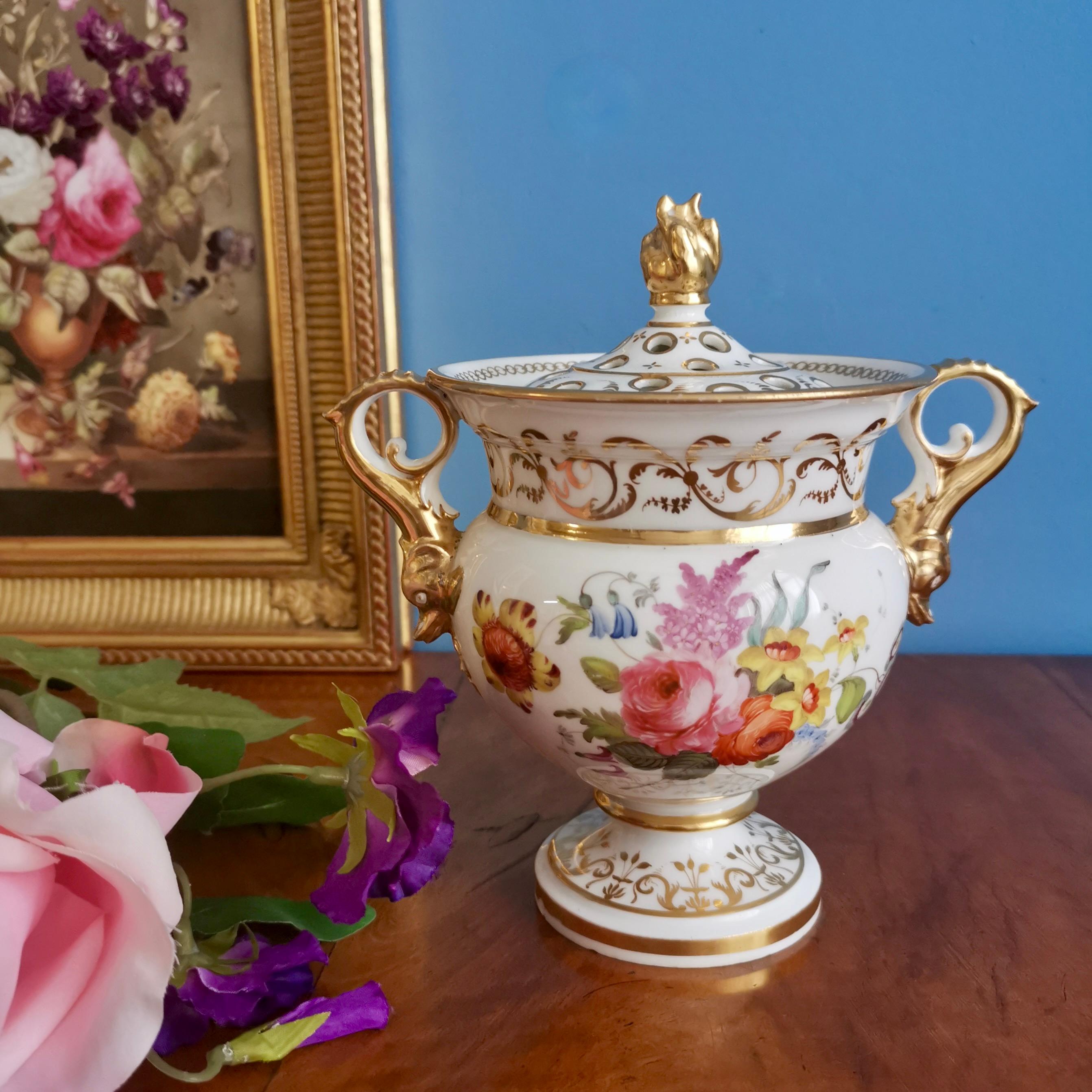 This is a gorgeous potpourri vase and cover made in England in around 1820. The vase has a simple white ground, stunning hand-painted flowers, a gilt flame finial and gilt dolphin handles. 

Potpourri vases were meant to hold a mix of scented