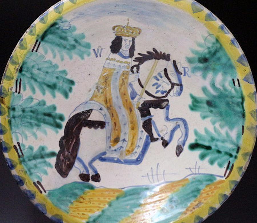 English delftware polychrome blue dash border charger with the image of the monarch King William riding on horseback. The portrait is flanked by the letters 