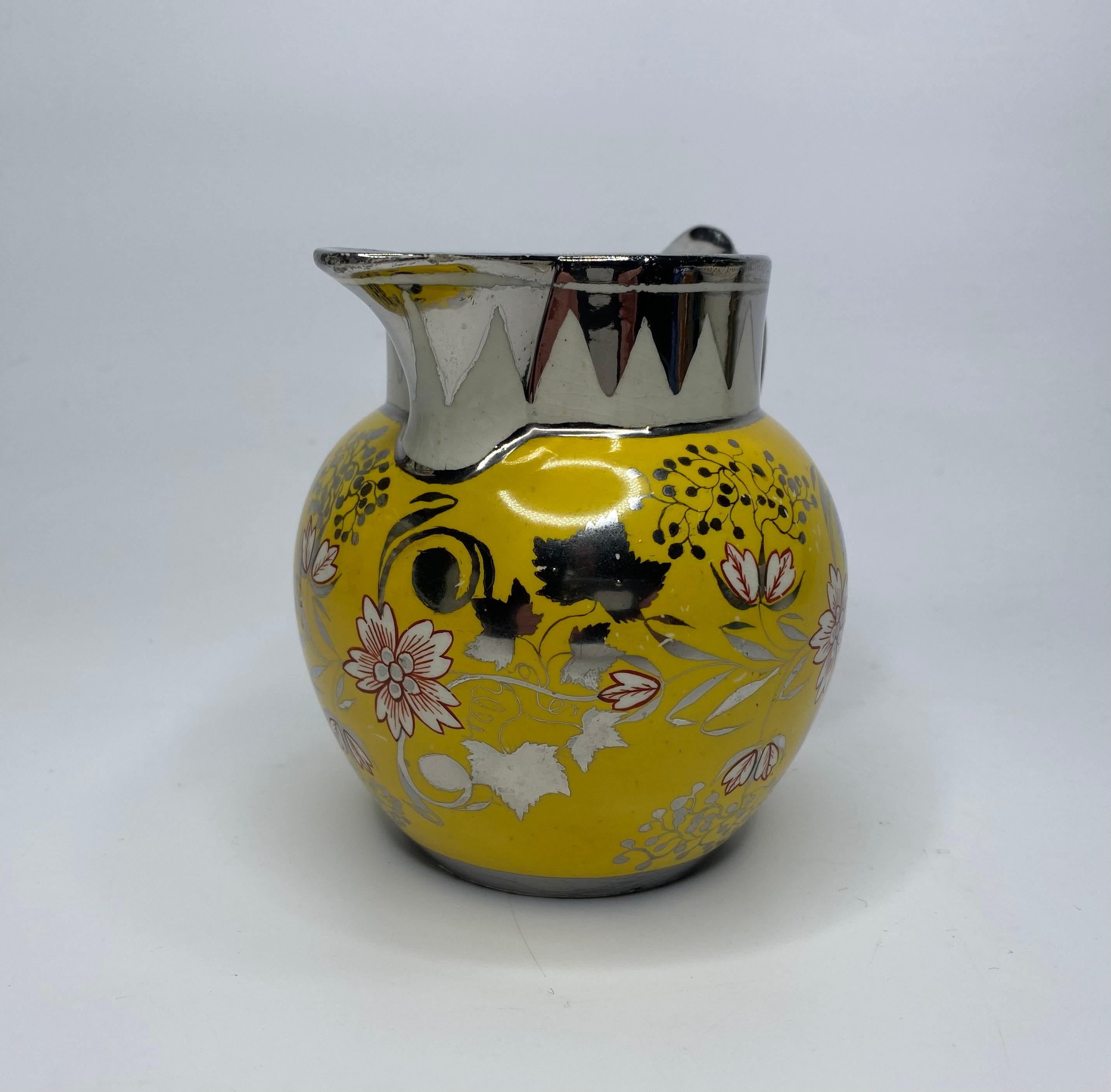 Staffordshire or Yorkshire pottery ‘Canary Yellow’ and silver lustre jug, c. 1820. The globular body decorated in silver lustre with a continuous band of stylised floral scroll, heightened in iron red, on a yellow ground; beneath a silver lustre