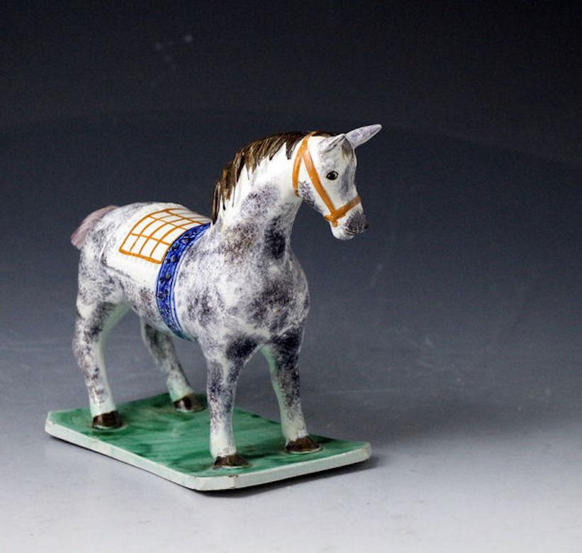 An exceptionally rare pottery figure of a fat-bellied sponge decorated grey horse modeled wearing a check blanket and a blue girth strap and standing on a translucent green base. This unusual version has good attention to details such as the horse's