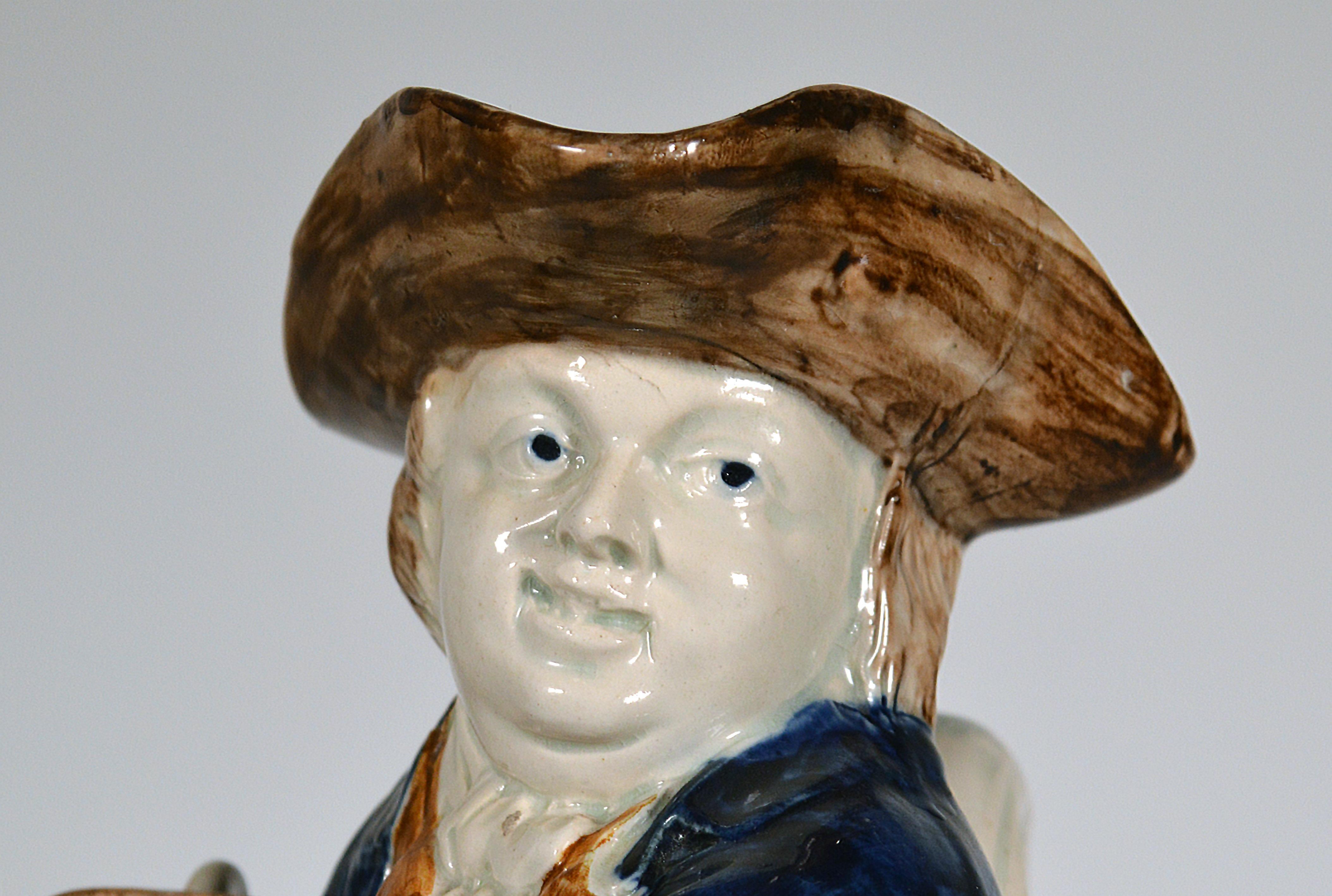 English pottery hearty good fellow pearlware toby jug
circa 1800
   

An unusual variation on the hearty good fellow standing toby jug, The base in white with the Toby figure standing, supporting a large white jug under his right arm, and