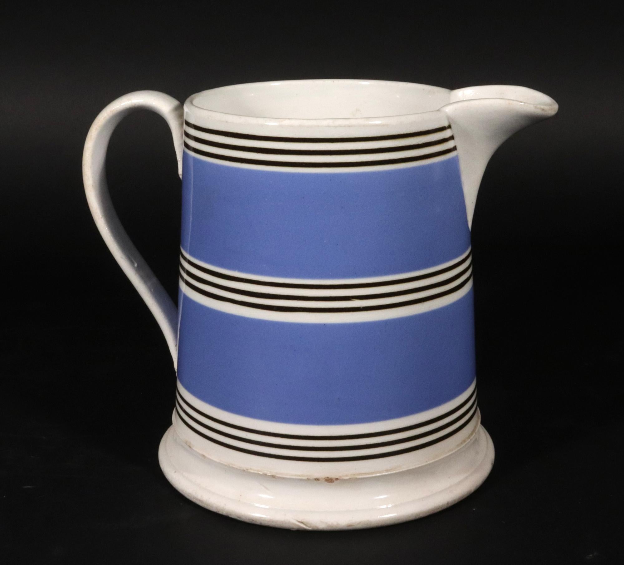 Pichet bleu moka,
Vers 1820-40

La cruche circulaire en poterie anglaise à engobe bleu, avec une base évasée et une anse en boucle avec des terminaisons en forme de feuilles.  La cruche avec un bec verseur. La cruche est entourée de trois bandes