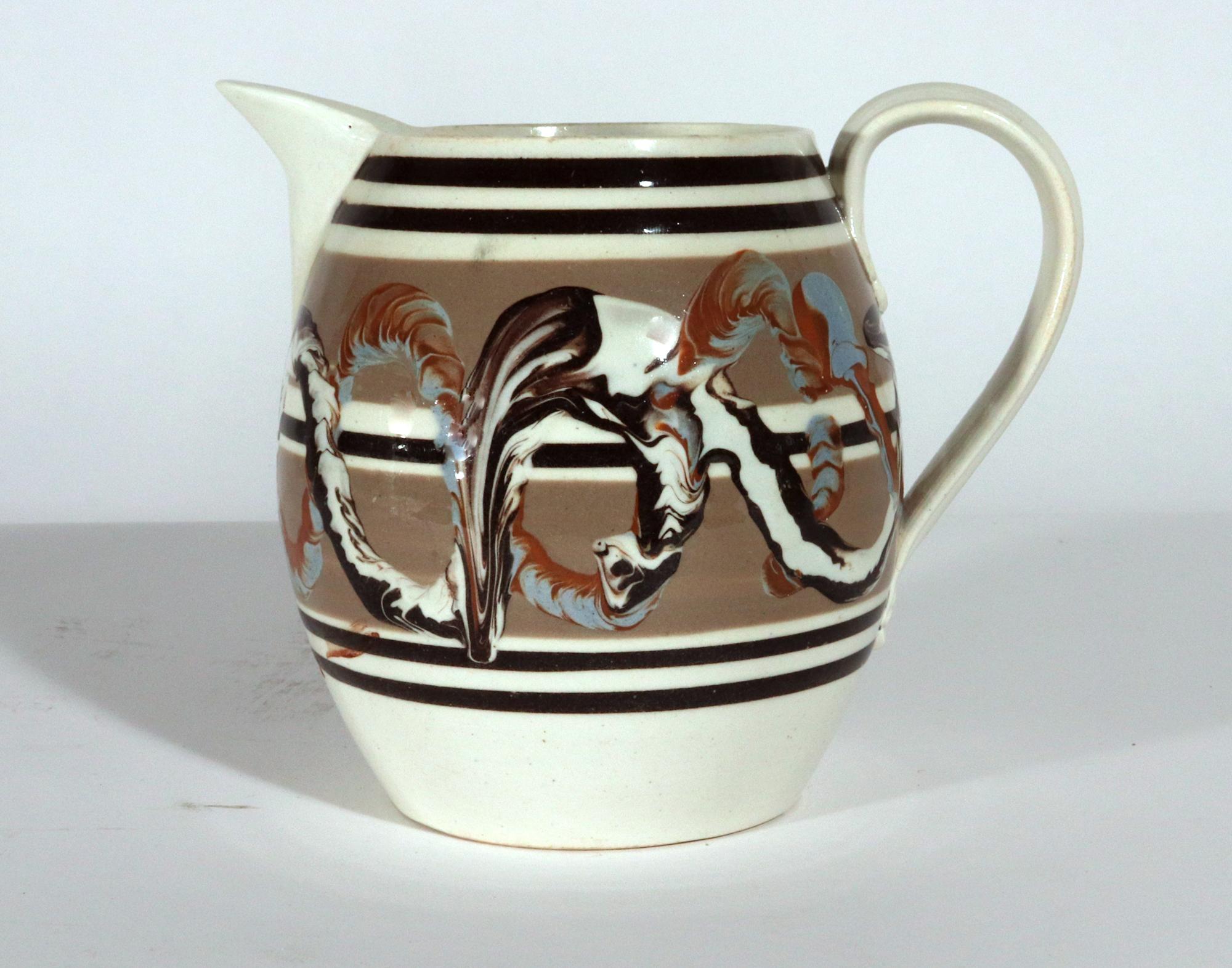 Mocha Creamware Double Earthworm Tankard,
Circa 1800

The mocha creamware jug is encircled by two different bands of the earthworm design.  One band is in an unusual red and blue and the other band is in brown and white which overlays the first