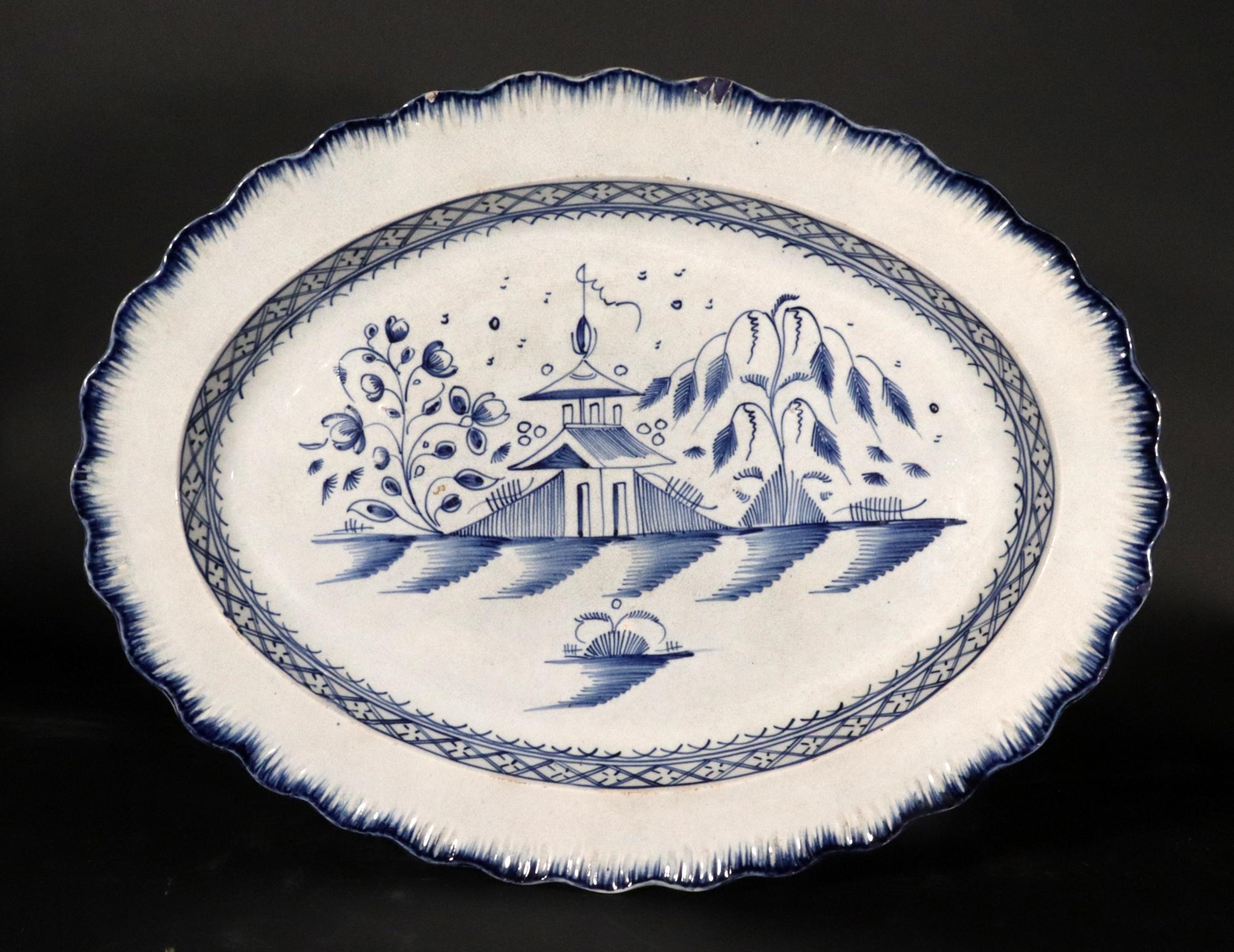 Piatto grande con bordo a conchiglia inglese Pearlware Blue Chinoiserie,
Variazione del modello China House,
Probabilmente Staffordshire,
Circa 1810

Il piatto in perle, con bordo a conchiglia modellato, è dipinto in blu sottosmalto con un paesaggio