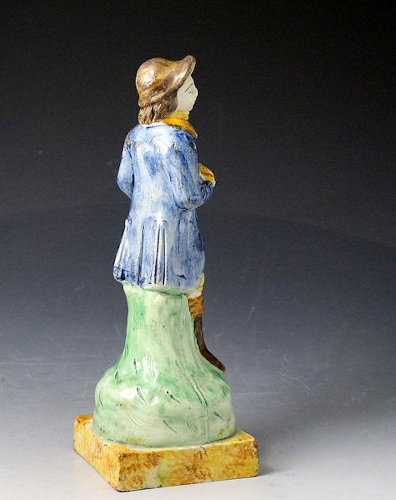 Dated: 1790-1810 England

An English pottery figure of a rural sportsman holding a resting gun and game bird. The character is modeled standing on a green mound on a square plinth base. The figure is strongly decorated in Prattware colors.