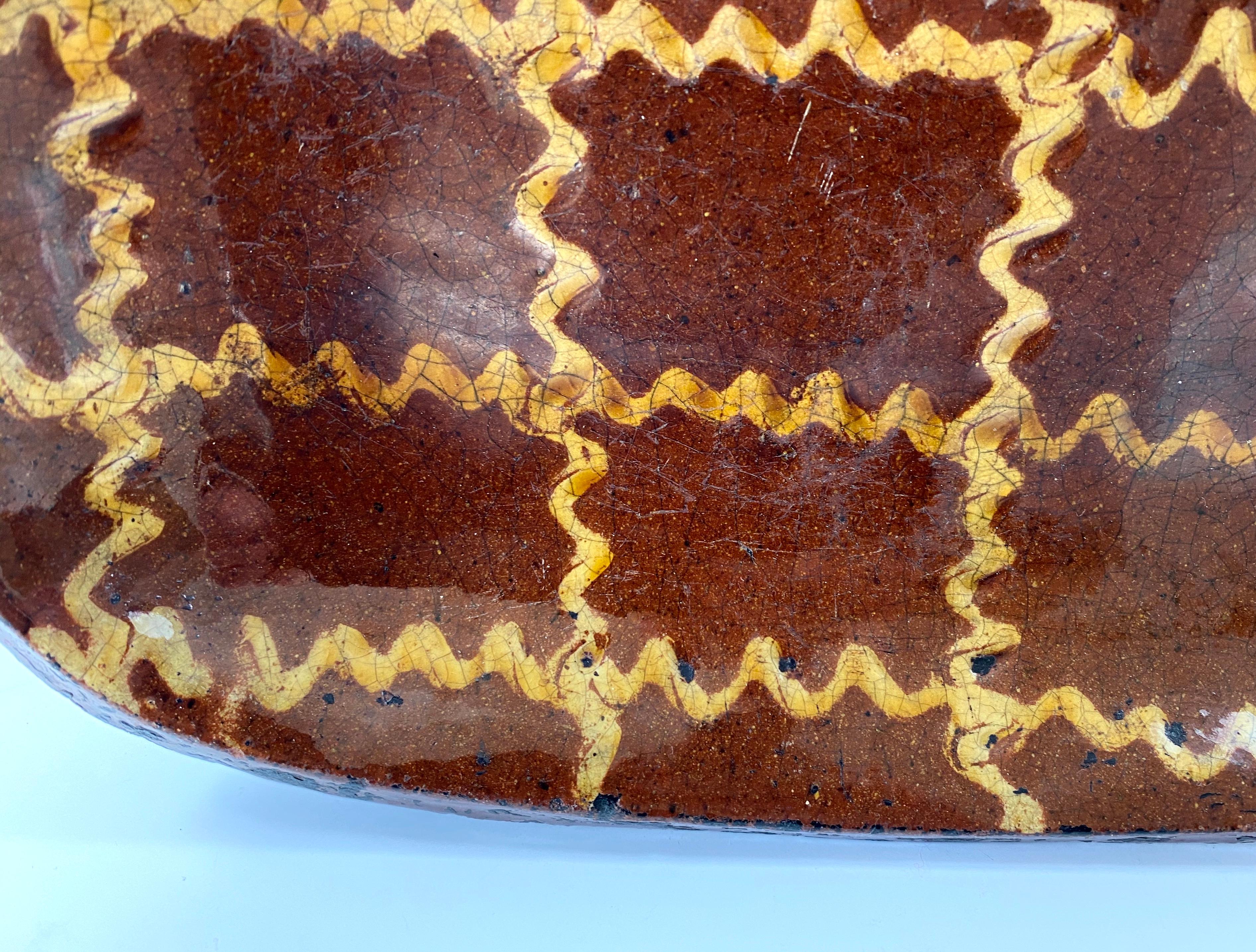 English pottery slipware baking dish, late 18th century. The plain edged, brown glazed dish, trailed in creamy yellow slip, with a wriggled, trellis design, beneath a thick, crazed glaze.
The underside baked black.
Staffordshire or Northern