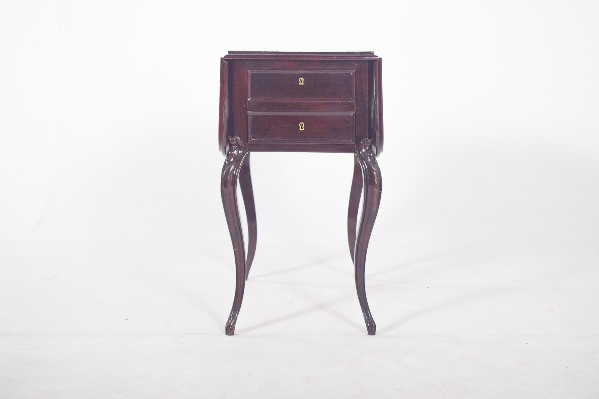 Potty table with flaps. In dark wood, with a folding top and two drawers at the front. The structure consists of four curved legs, with notches at the upper joints. The interior reveals its original function, a chamber pot compartment, with a
