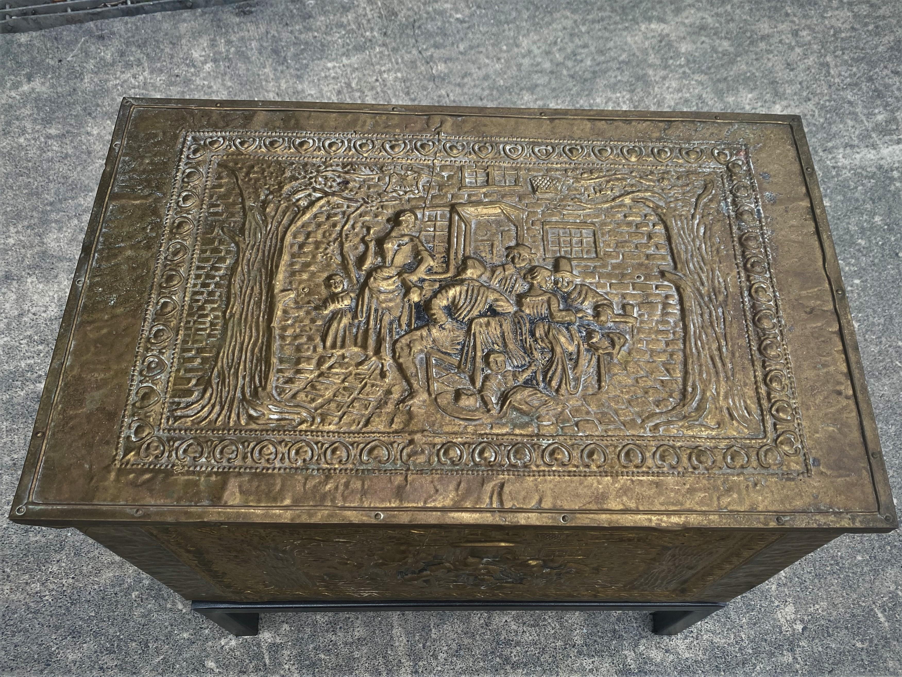 Here is a decorative and functional pressed brass lift lid box with a zinc liner and an iron base which has been added. The top and front have an impressed scene depicting a group who appear to be eating and drinking in front of a brick building and