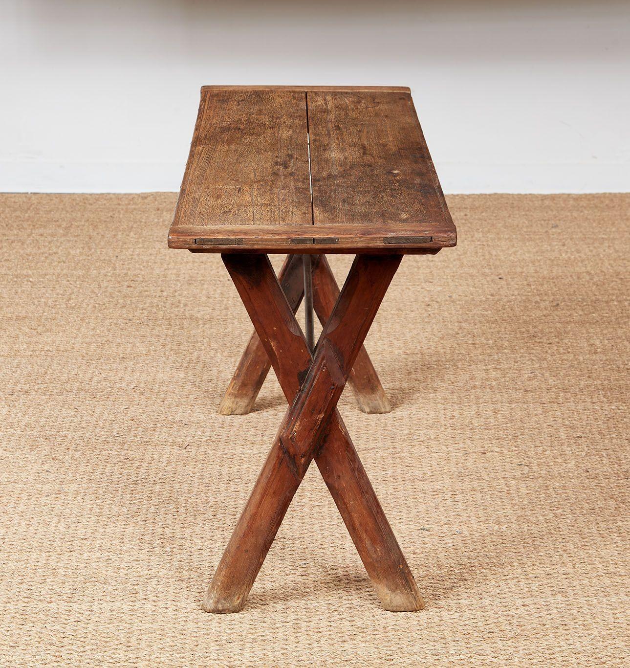 An X-frame English pub table in pine, the trestle base with chamfered legs and original iron stretcher, and the scrubbed top with breadboard ends and through-tenon construction, the surface showing the wonderful wear of many a game and pint.   Now