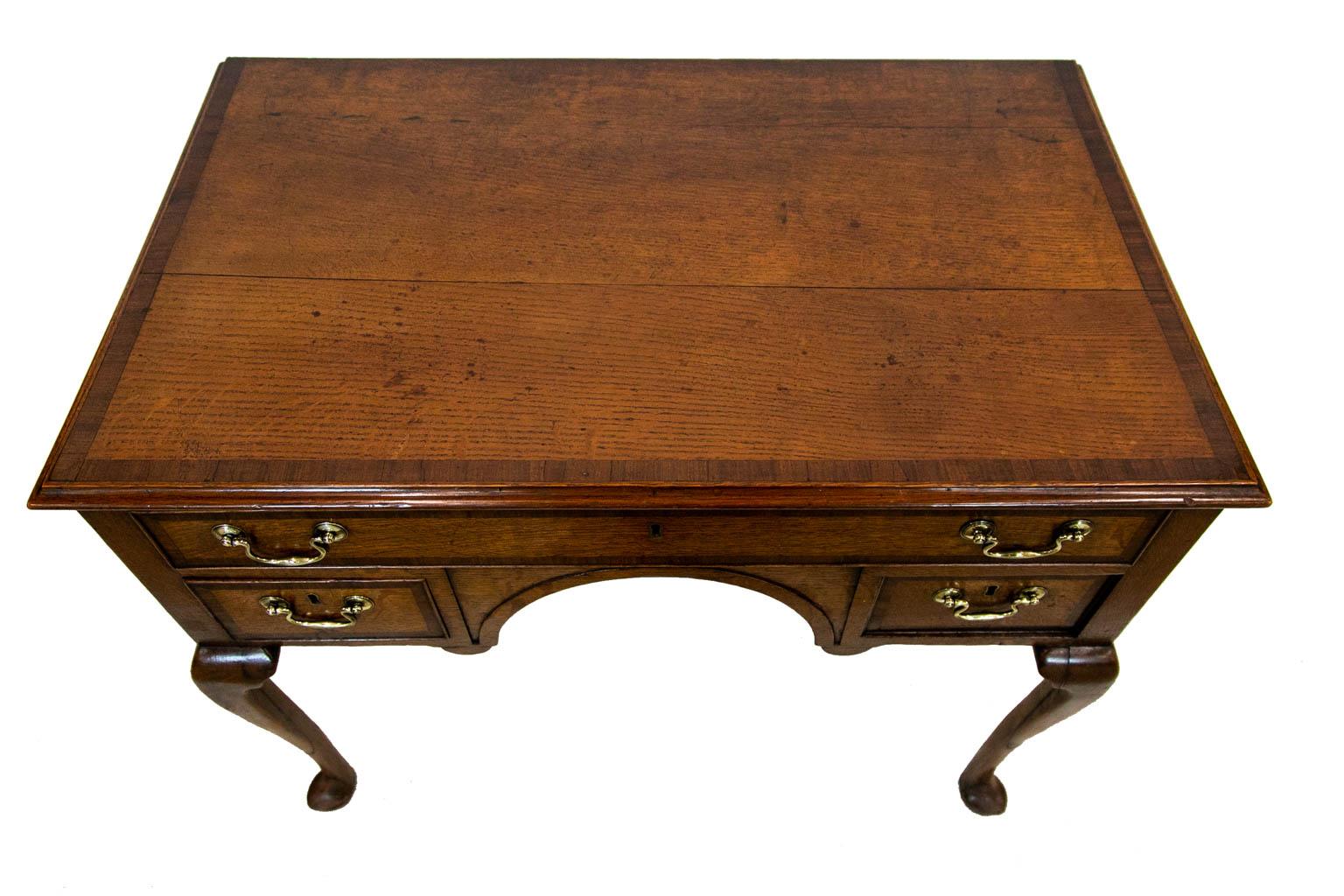 This oak and mahogany lowboy has a 1/16 inch shrinkage separation in the top. The top has an applied ogee molding and is crossbanded with 3/4 inch mahogany crossbanding. The drawer fronts have a 1/2 inch mahogany crossbanding with the original brass
