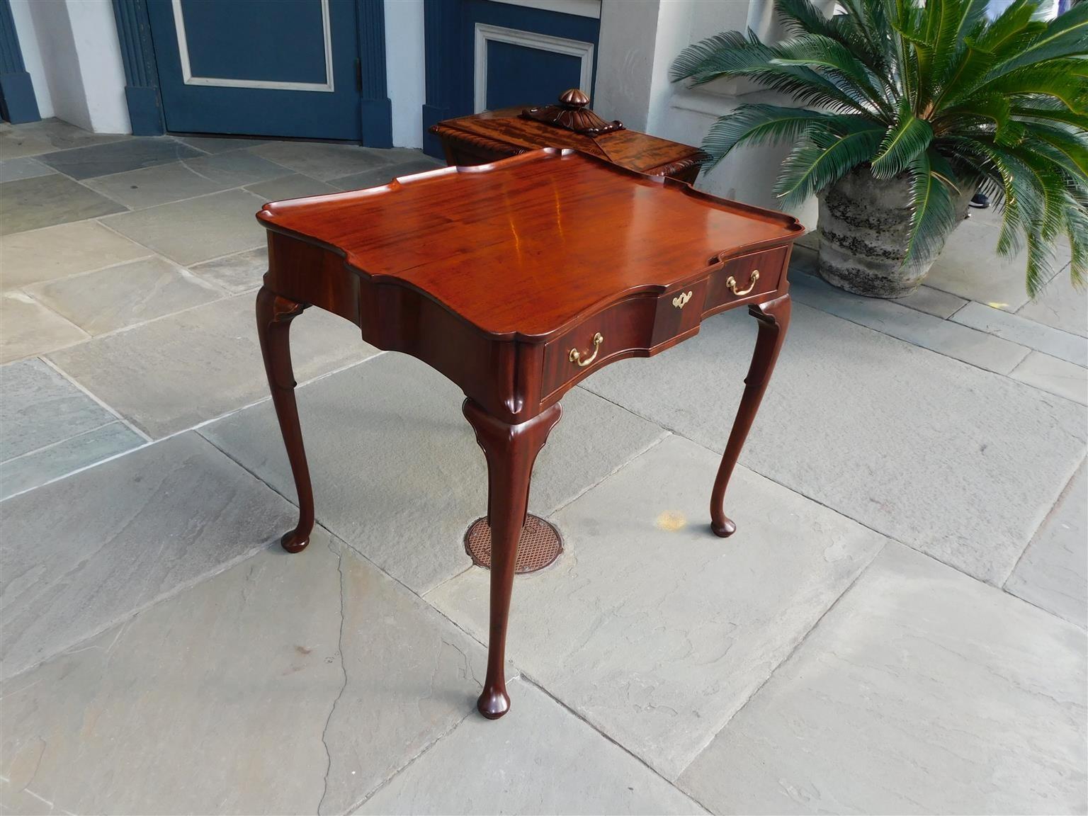 English Queen Anne mahogany one drawer tea table with a one board serpentine edge top, original brasses, trumpet knees, and resting on cabriole legs with pad feet. Secondary wood is Oak. Early 18th century.