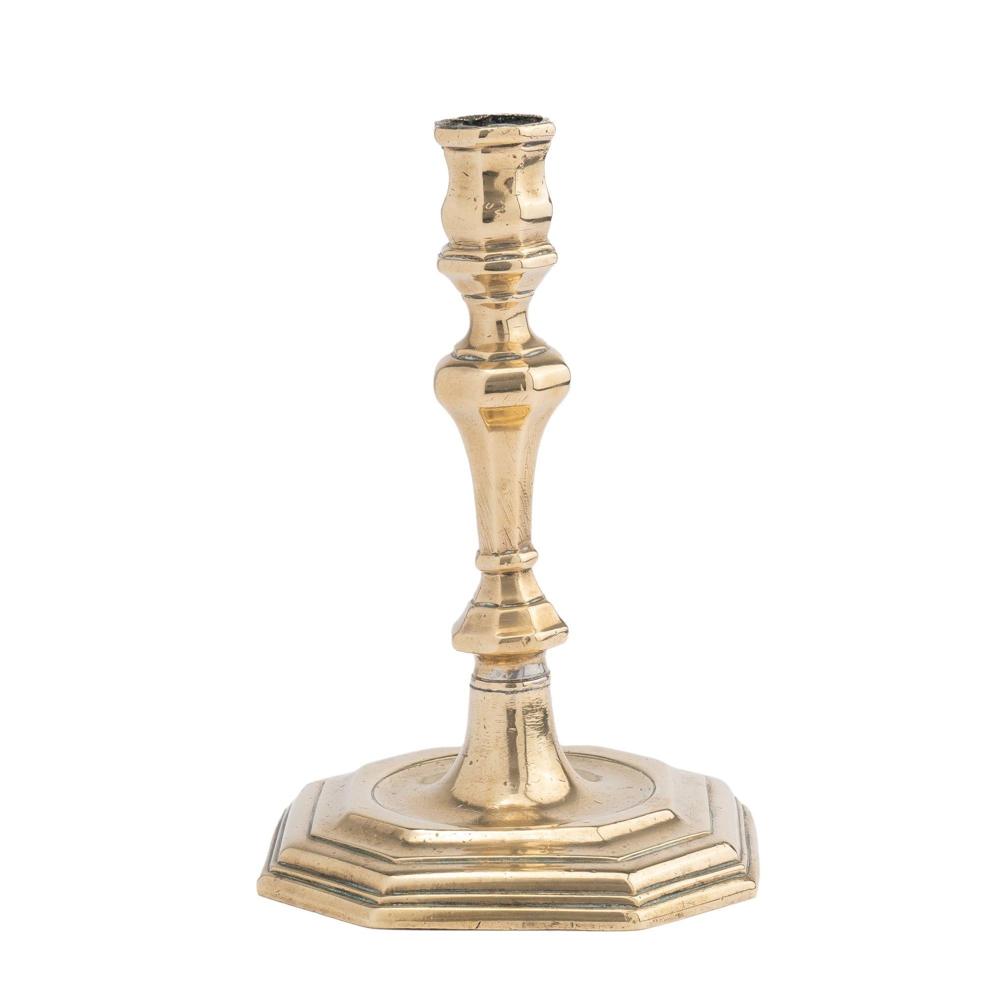 Core cast Queen Anne hexagonal base brass candlestick. The design features a hexagonal candle cup on a waisted pedestal, which sits above an hexagonal trumpet form shaft and suppressed hexagonal knob, peened to the conical center element to a