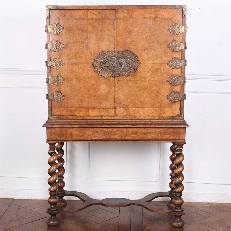 English Queen Anne-Revival cabinet on stand, the doors with book-matched burl walnut veneer and herringbone inlay and with ornate pierced brass hardware. Bold spiral-turned legs and 'X' stretcher. The doors open to reveal a painted green interior