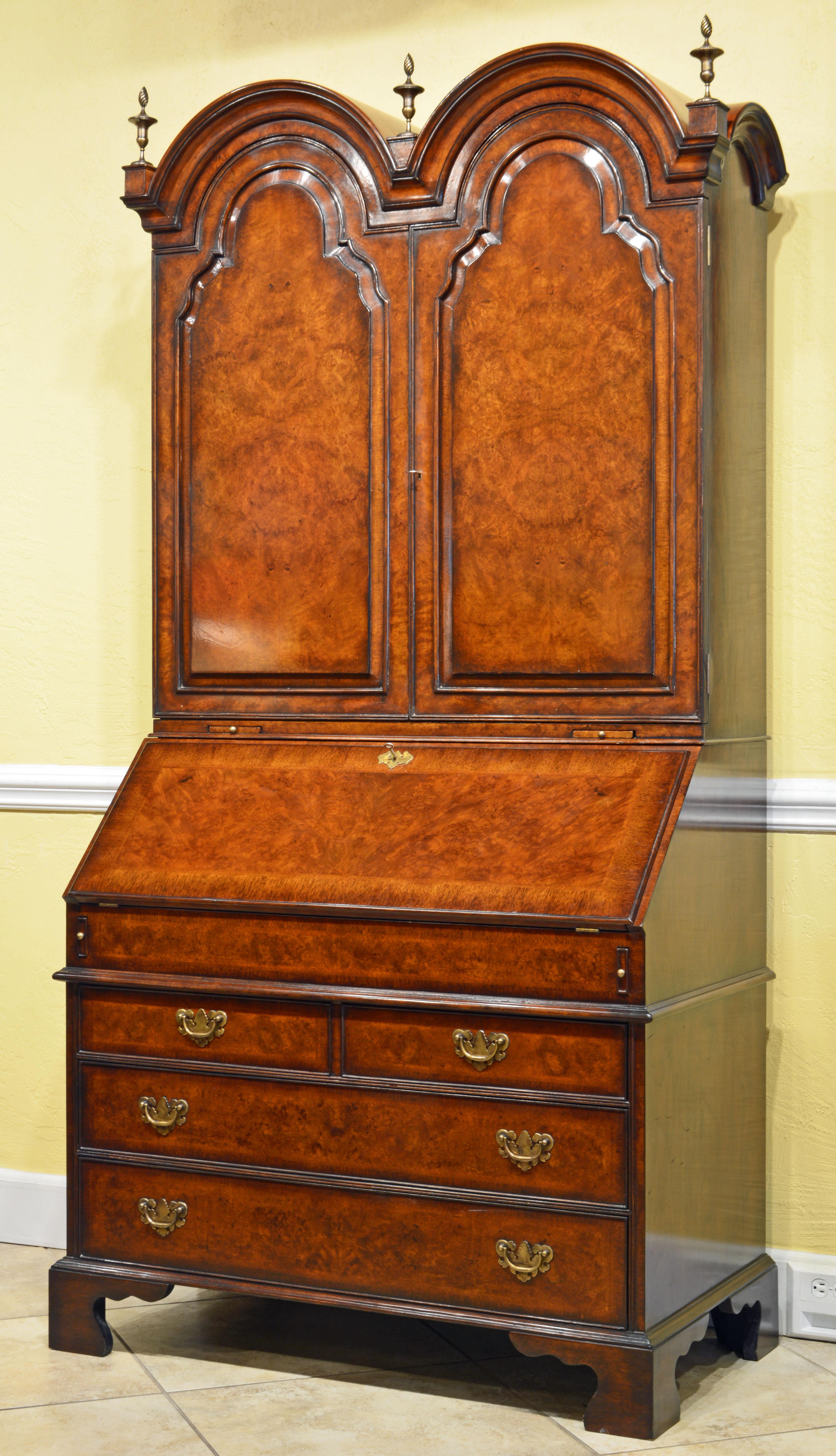 An English burled walnut Queen Anne style two part secretary desk with a double domed top and carved urn form brass finials. The wooden tombstone doors enclose a fully fitted interior with multiple drawers, pigeon holes, document compartments,