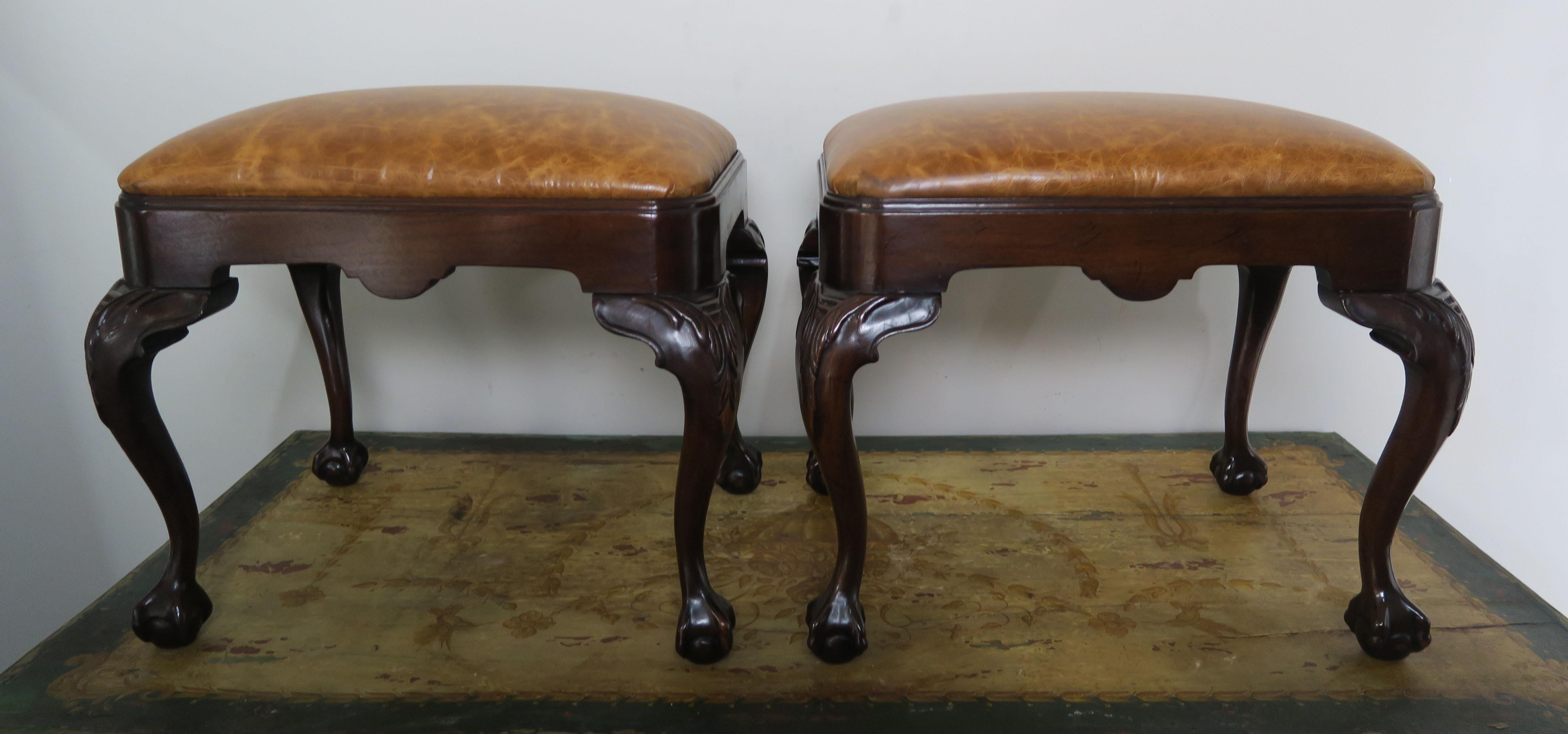 Pair of English early 20th century Queen Anne style mahogany benches newly upholstered in leather. The beautifully carved benches stand on four cabriole legs that end in claw and ball feet. A handsome pair for any Traditional style decor.