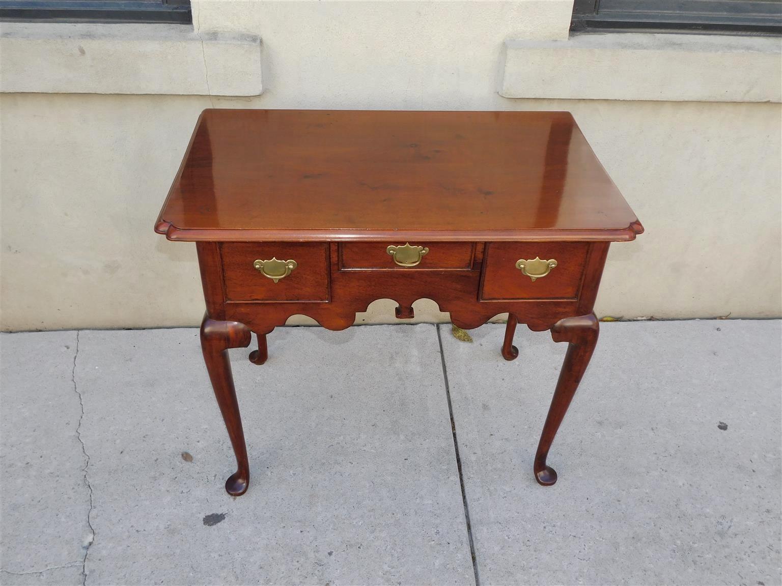 English Queen Anne Walnut three drawer lowboy with an incised molded edge top, carved scalloped skirt, original brasses, and resting on cabriole legs with pad feet, Early 18th Century