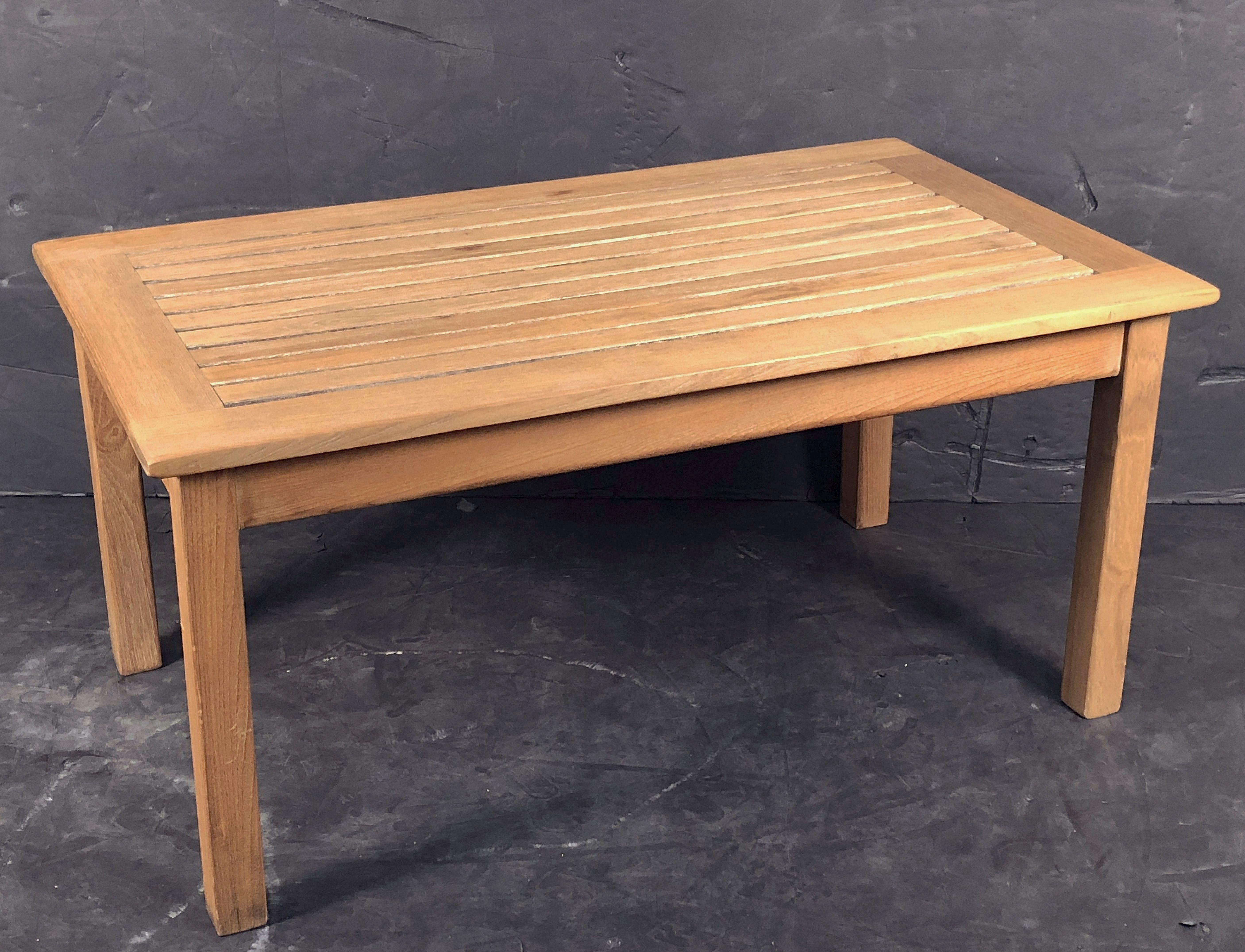 A fine English low or cocktail or coffee table of patinated teak for the garden or patio featuring a rectangular slatted top set upon a sturdy four-legged frame.