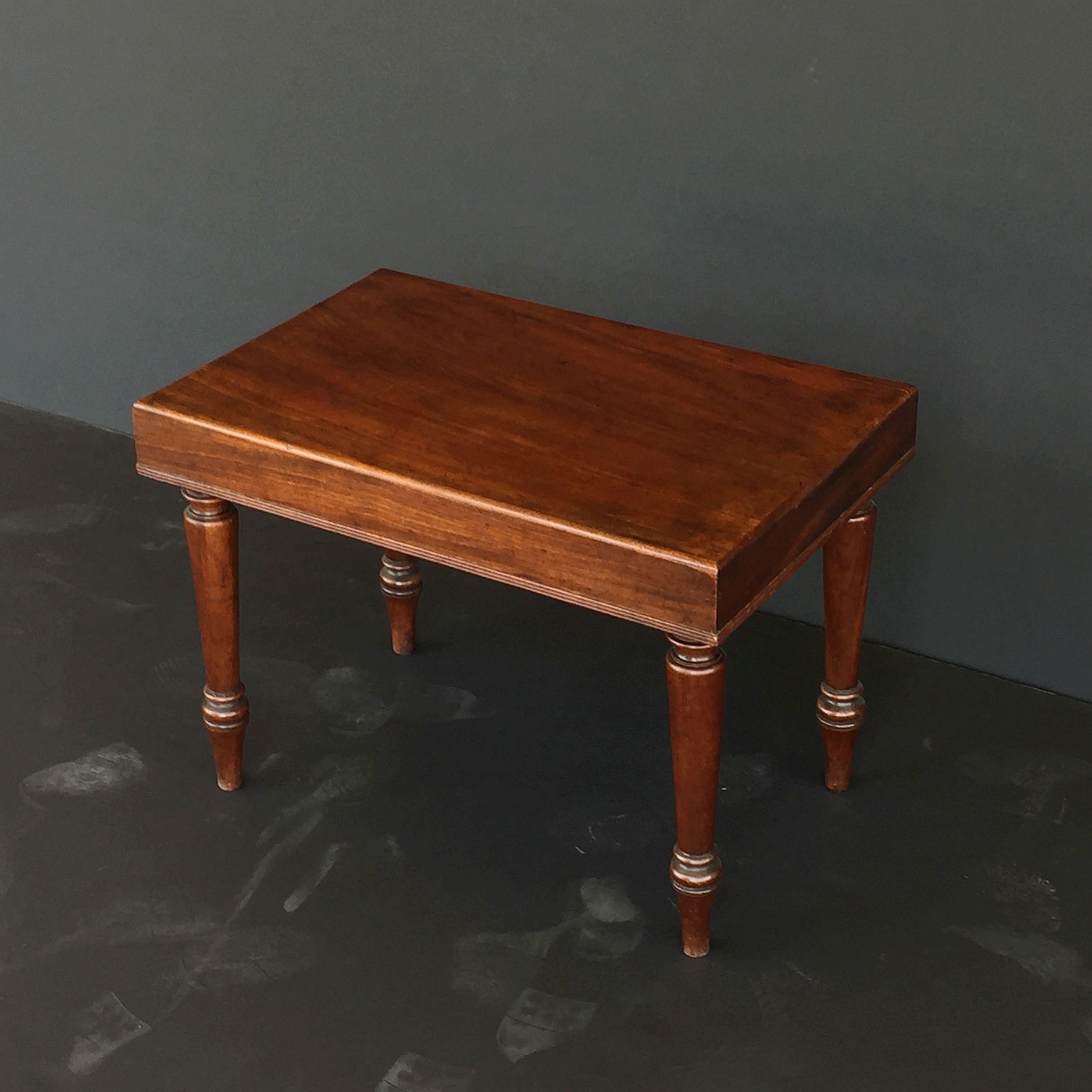 A fine English side or end table of mahogany from the 19th century, featuring a moulded rectangular top on four turned legs.