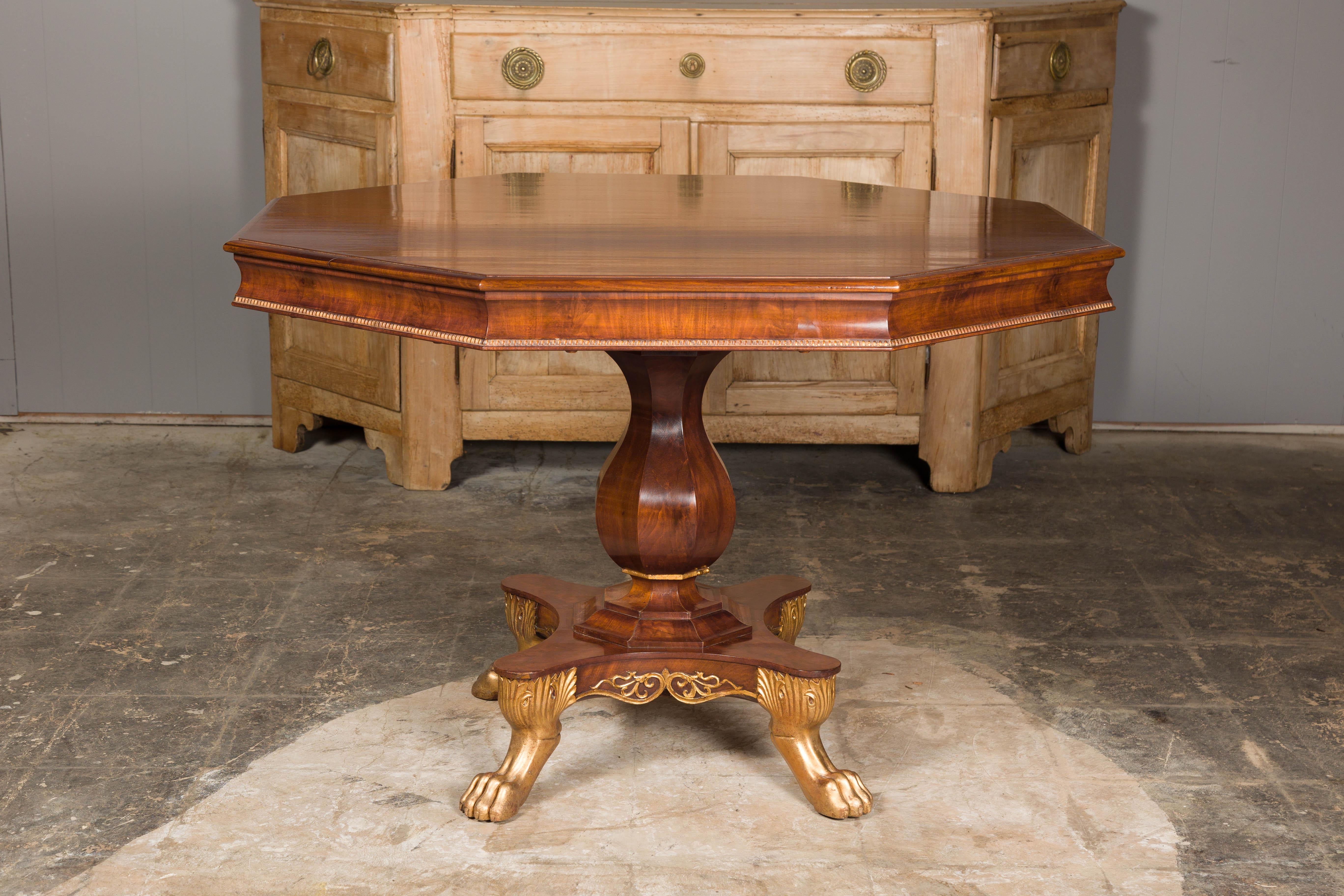 An English Regency period mahogany center table circa 1820 with octagonal top, carved pedestal and gilded lion paw feet. Enveloping the quintessence of the English Regency period, this mahogany center table, circa 1820, is a harmonious blend of