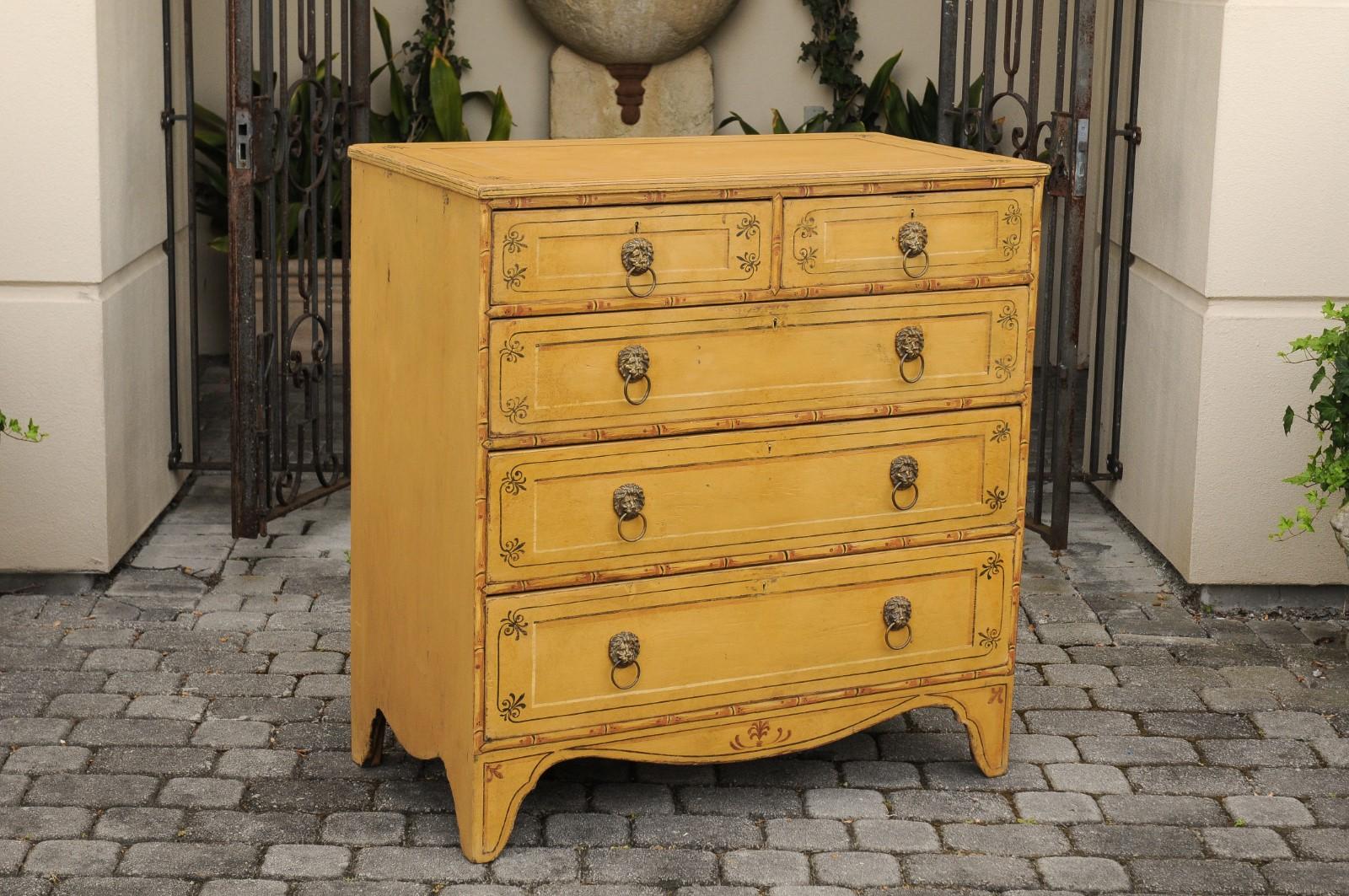 An English Regency goldenrod painted wood five-drawer chest from the 19th century, with floral accents and splayed bracket feet. Born in England during the first half of the 19th century, this English Regency painted commode features a rectangular