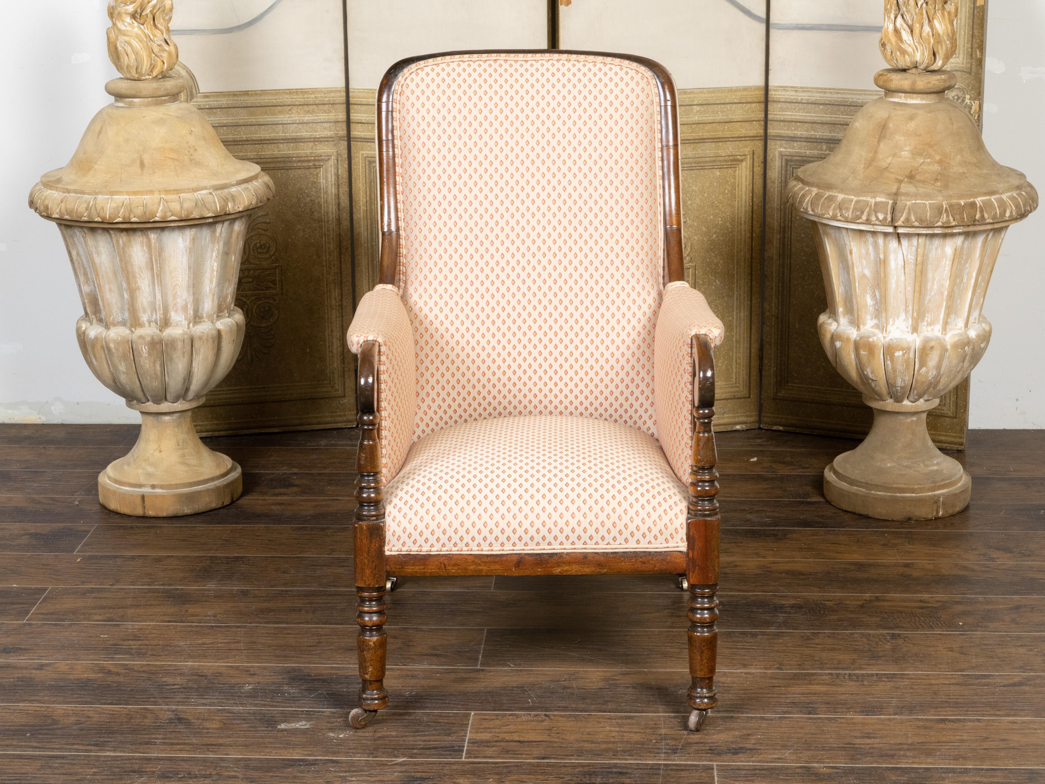 An English Regency period mahogany armchair from the early 19th century, with scrolling arms, turned legs, upholstery and petite casters. Created in England during the second quarter of the 19th century, this mahogany armchair features a straight