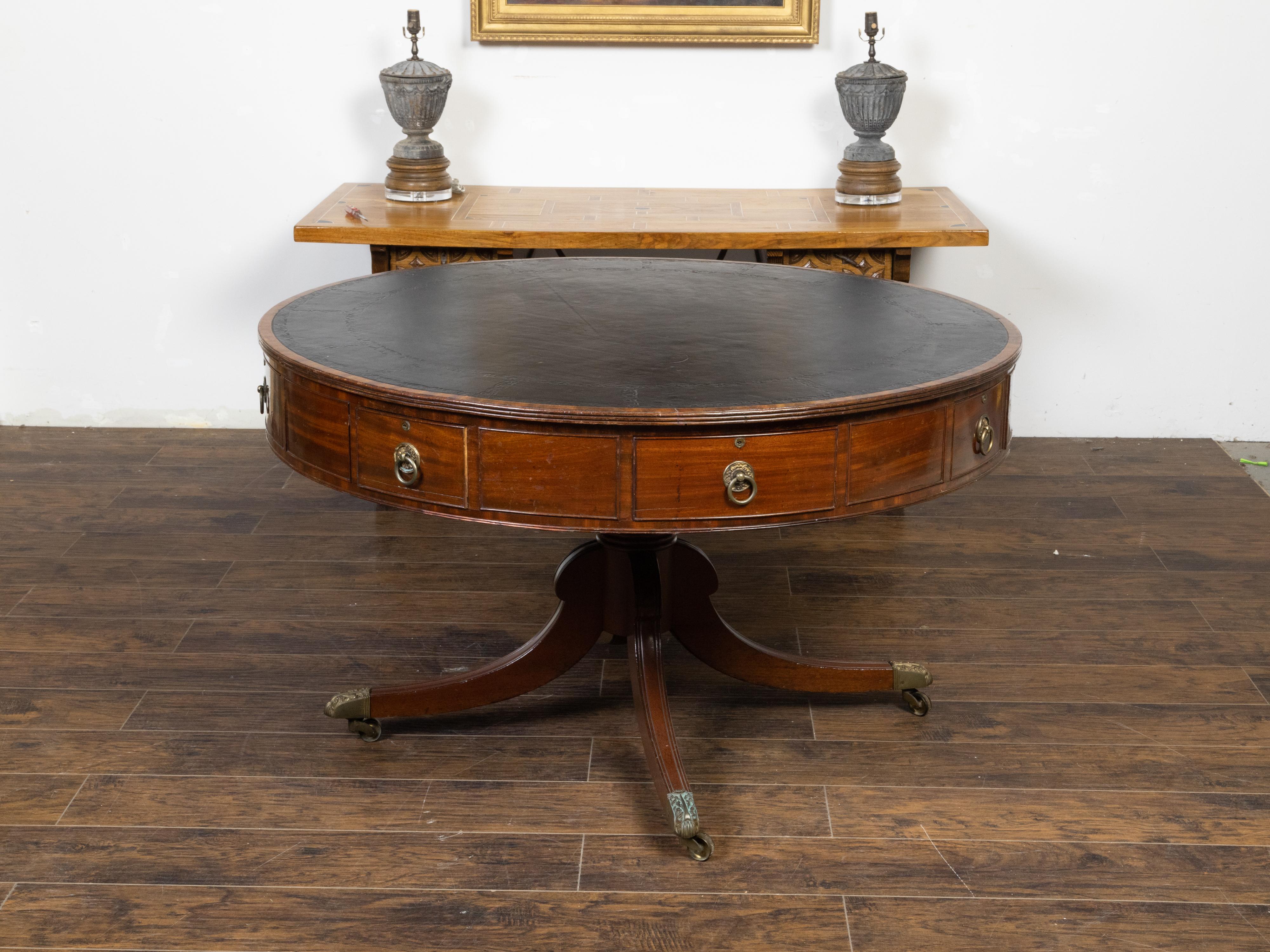 An English Regency period mahogany drum or rent table from the early 19th century, with black leather top, eight drawers, pedestal and quadripartite base on bronze feet. Created in England during the second quarter of the 19th century, this Regency
