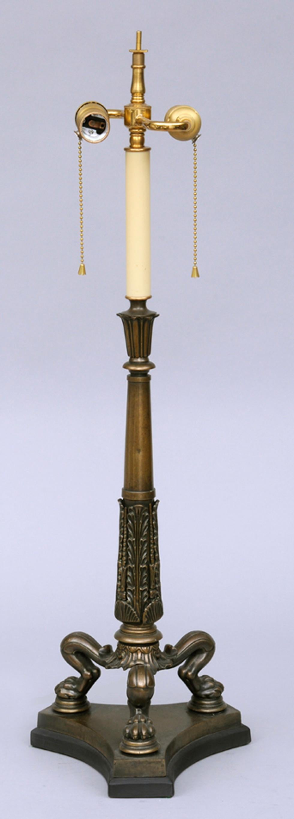 Regency bronze lamp with tall foliate and shell patterned column, tripod paw feet on concave-shaped base with black paper shade.