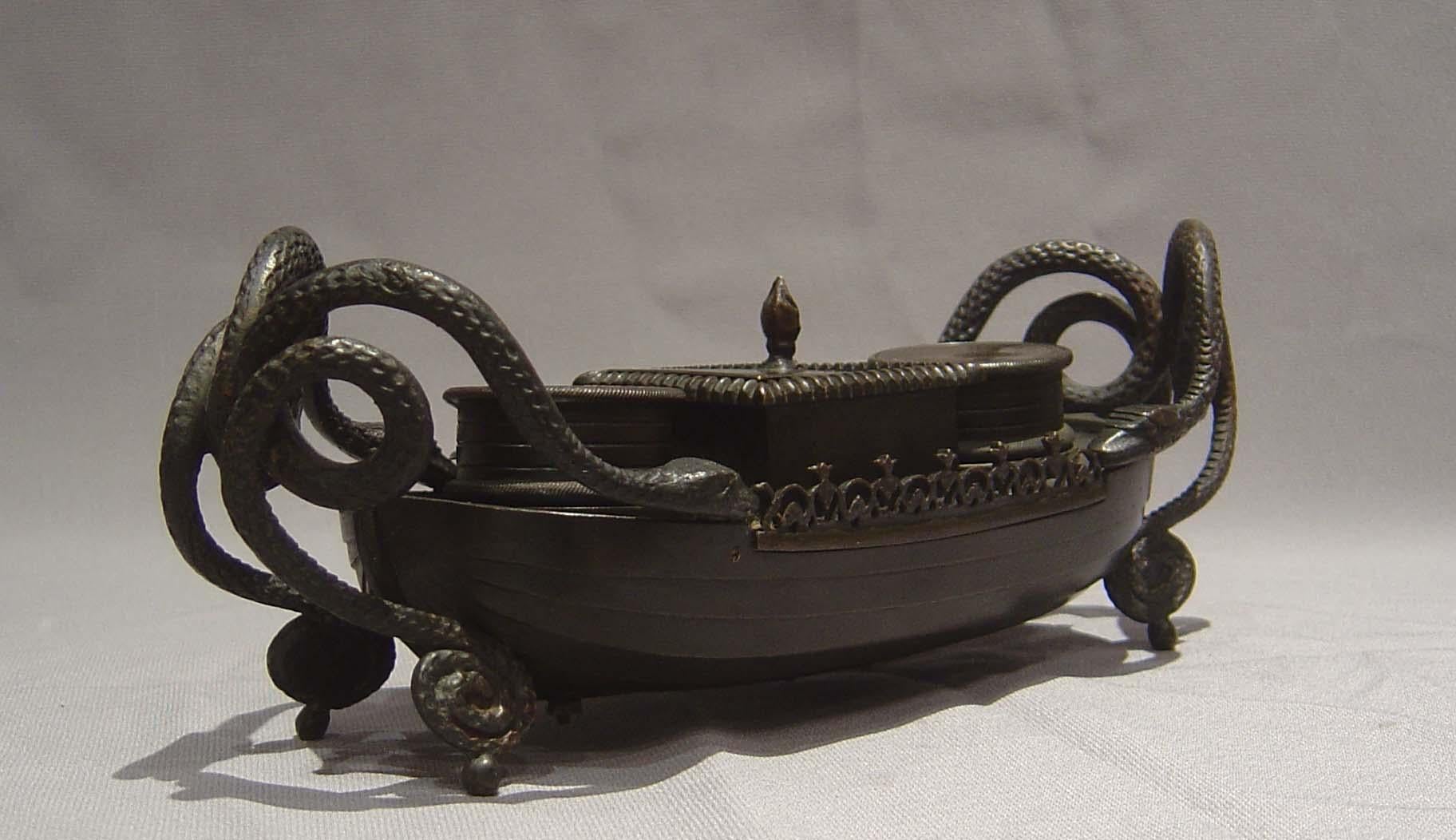 A fine English Regency period patinated bronze inkwell in the shape of a long ship. The main body of the inkwell is in the form of a ship and in a form of shipbuilding known as clinker built where the planks are not laid edge to edge but where the