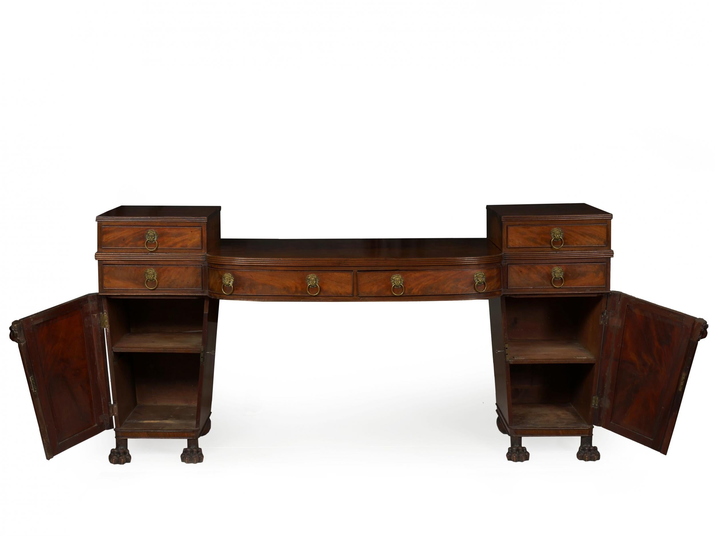 A powerful architectural sideboard from the first quarter of the 19th century, it is characterized by a pair of drawer boxes over a pair of drawers flanking a demilune serving surface with two conforming drawers over trapezoidal pedestals with four