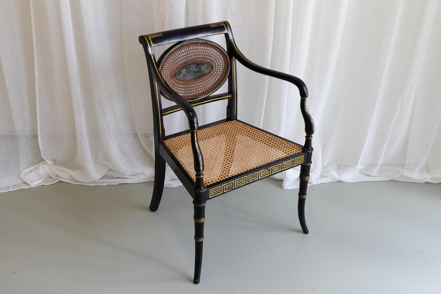 English Regency Black and Gold Armchair, 19th Century.

Antique shield back chair with hand painted cherub/putti motif. Ebonized frame with golden Greek key patterns and striping.  Woven cane seat and back. Turned curved front legs. 

Good original