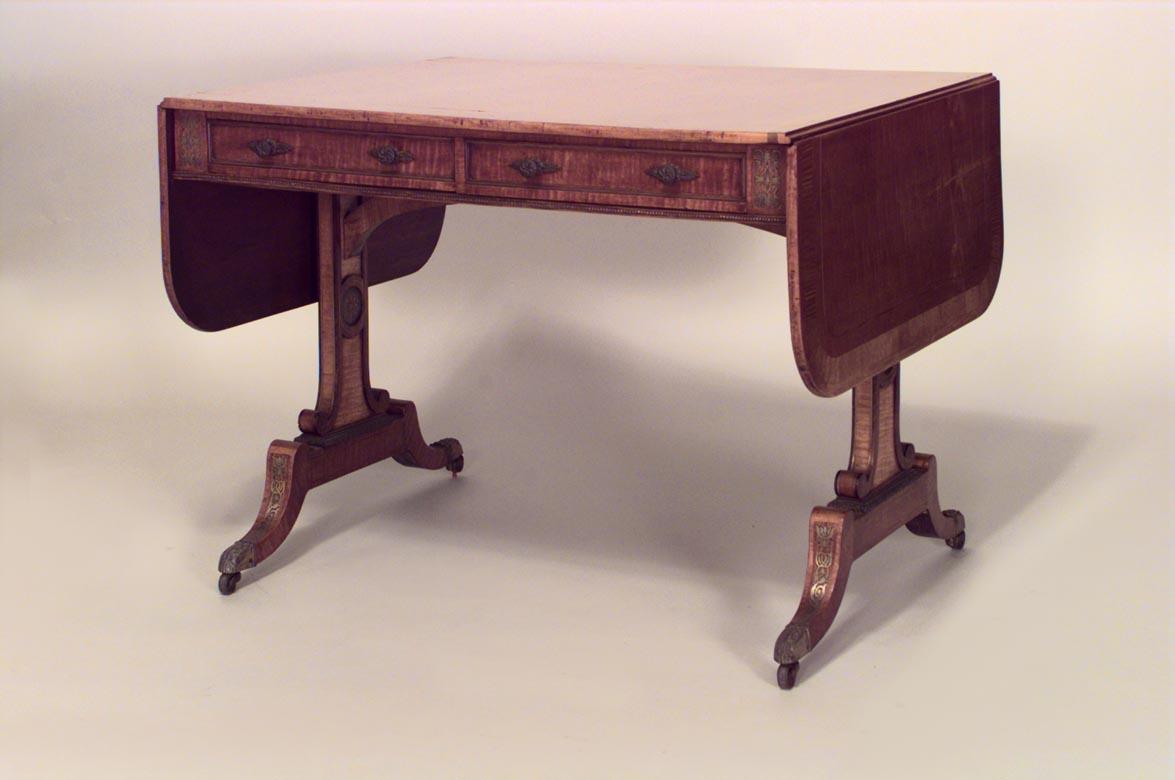 English Regency (c. 1815) brass inlaid & mounted satinwood sofa table with tulipwood cross-banded top above 2 frieze drawers on trestle legs with brass caps & casters.
