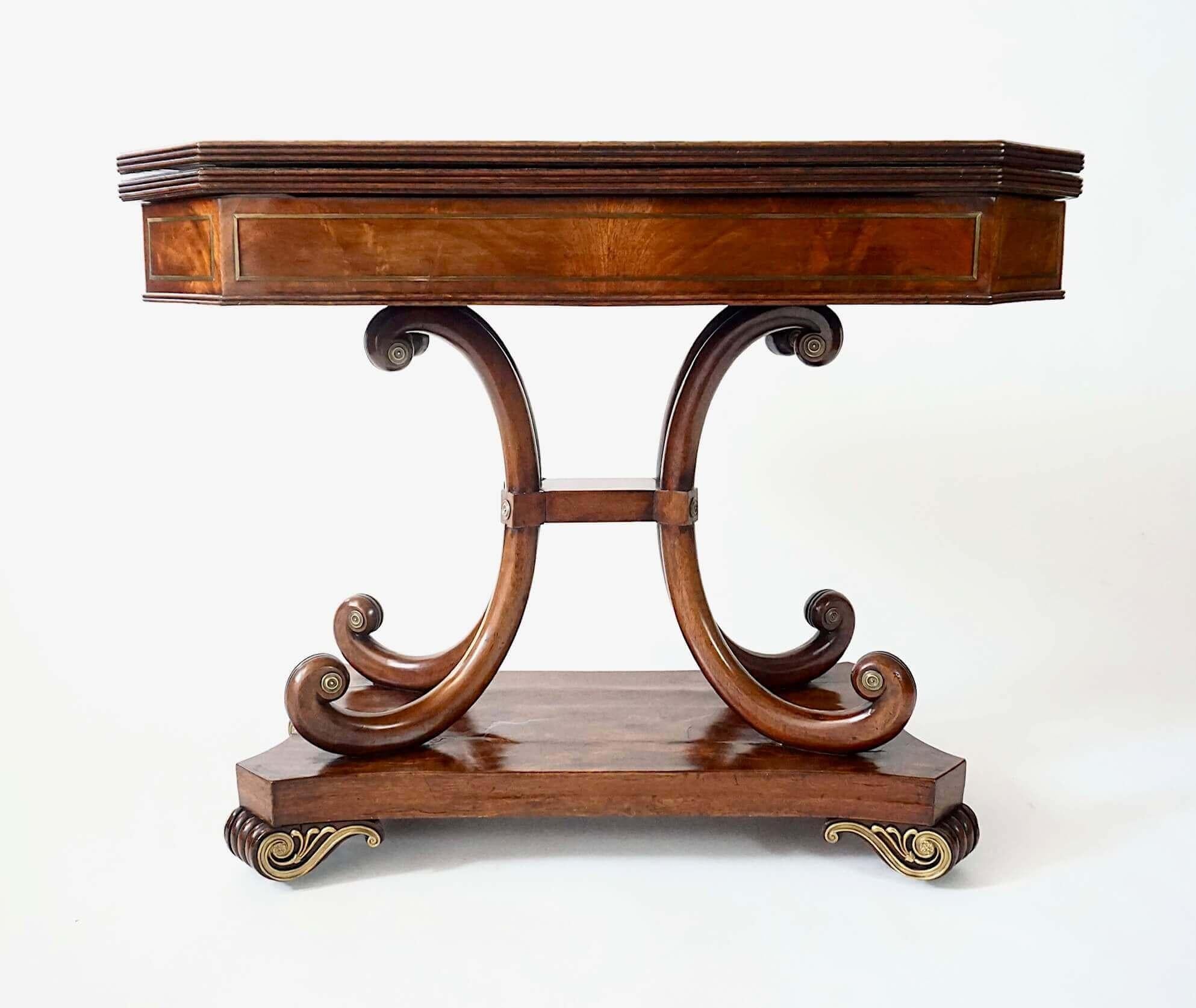 An exceptionally fine and elegant circa 1815 English George III regency period console table of unusual design and striking mahogany veneers, the rectangular reeded-edge fold-over top with canted front corners, brass line inlay borders, and