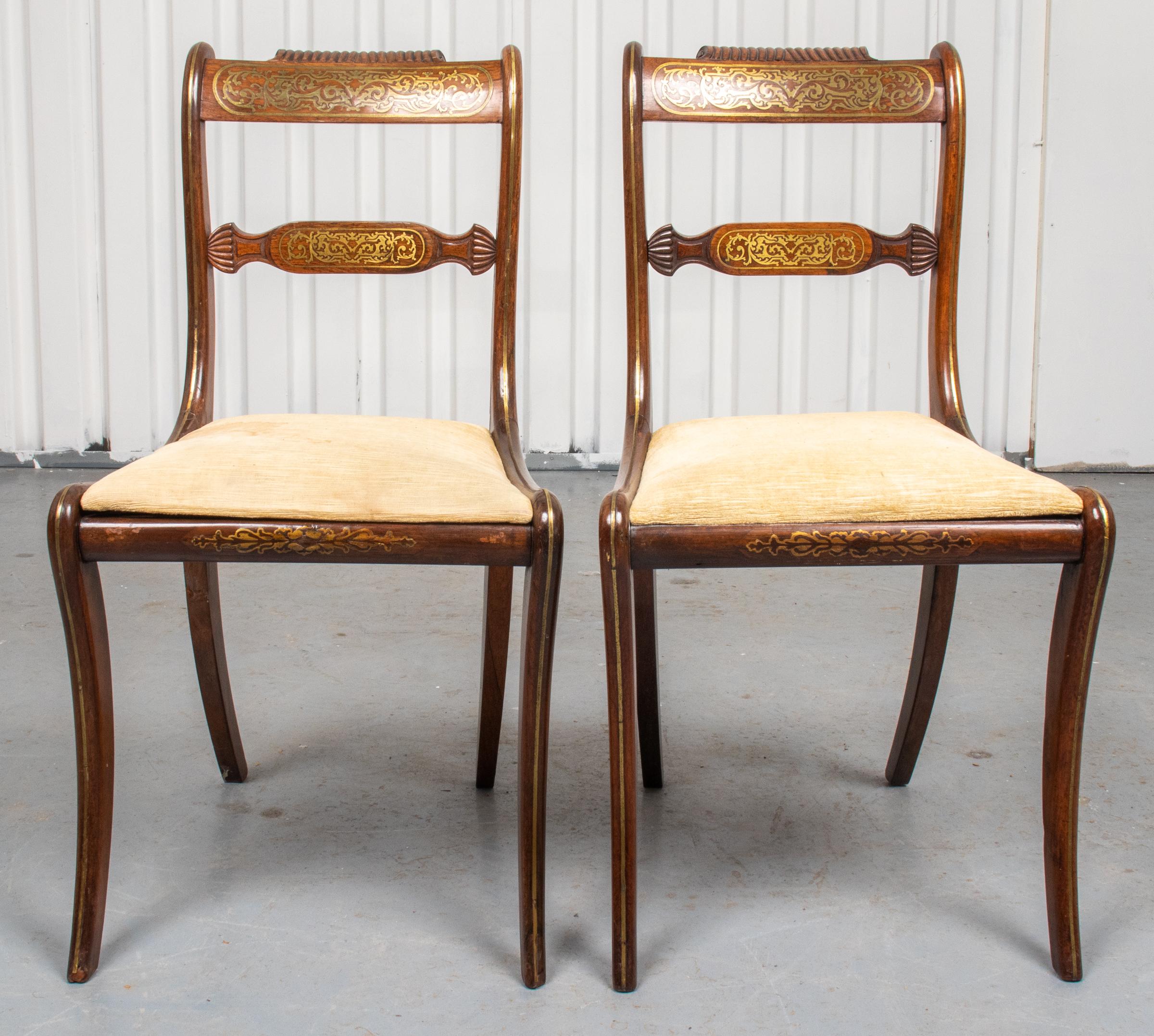 Pair of Regency brass inlaid side chairs, early 19th century, the carved crest rail above brass inlaid panels, the seat raised above curved saber legs. Measures: 33.25” H x 18” W x 21” D.
