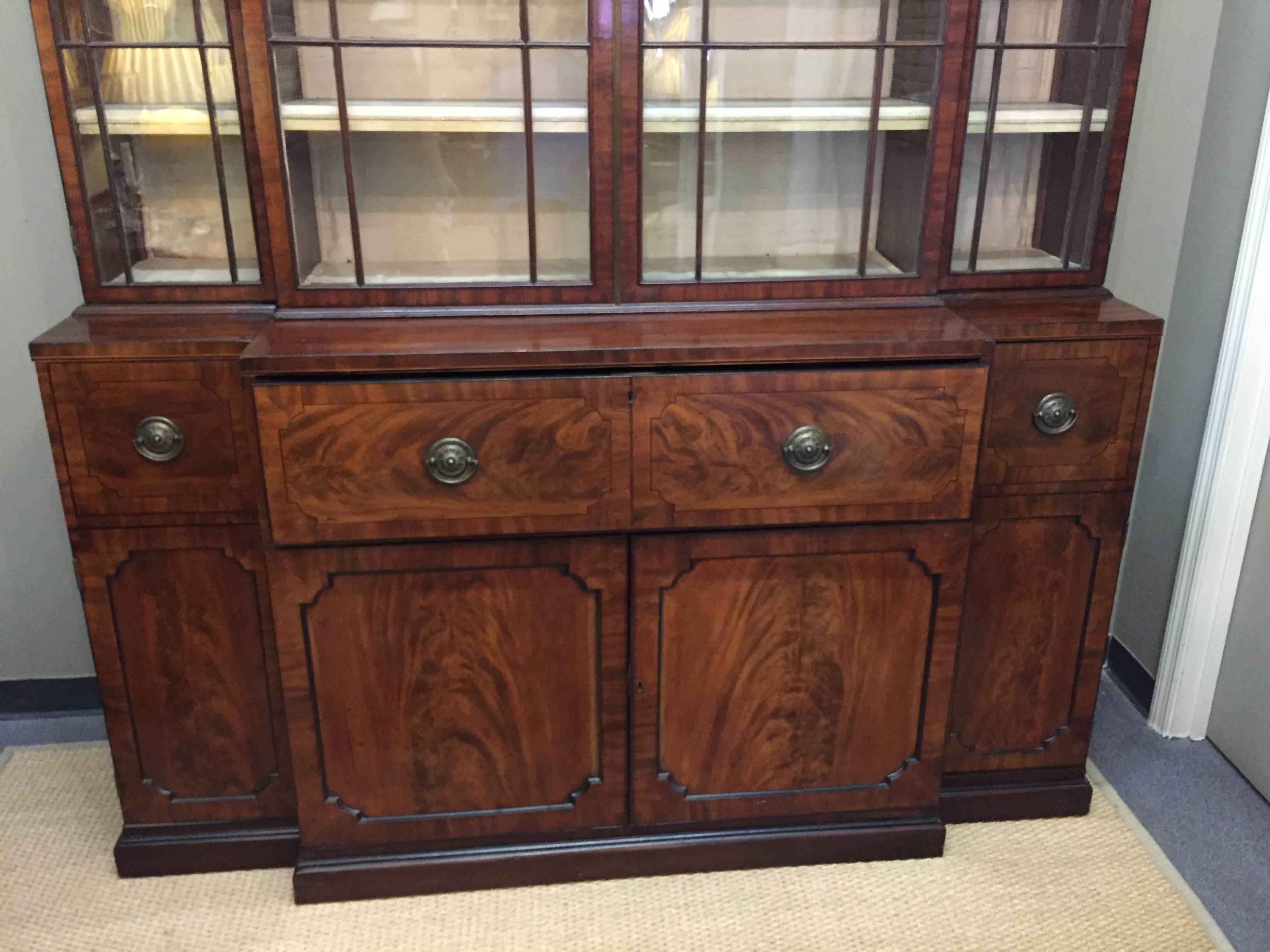 English Regency Breakfront in light crotched mahogany. Secretary interior with satinwood drawers and burgundy leather writing surface. Beautiful window pattern with dividers, adjustable shelves, interior drawers with campaign pulls. Six-piece