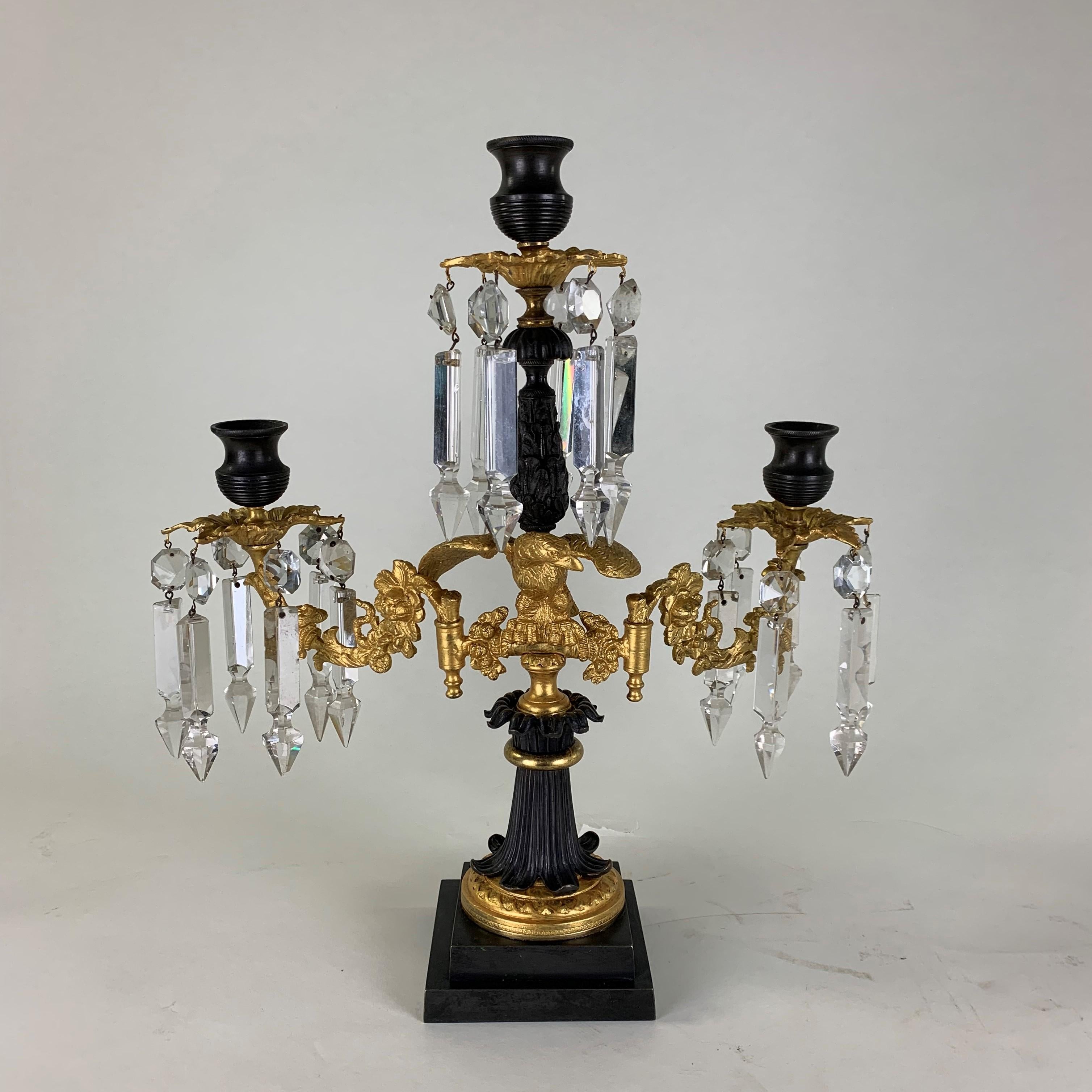 A very fine quality early 19th century English bronze & ormolu three branch candelabra. Each branch has a shaped bronze candleholder above gilded drip pans adorned with prismatic cut-glass drops. set on a central gilt eagle with outstretched wings