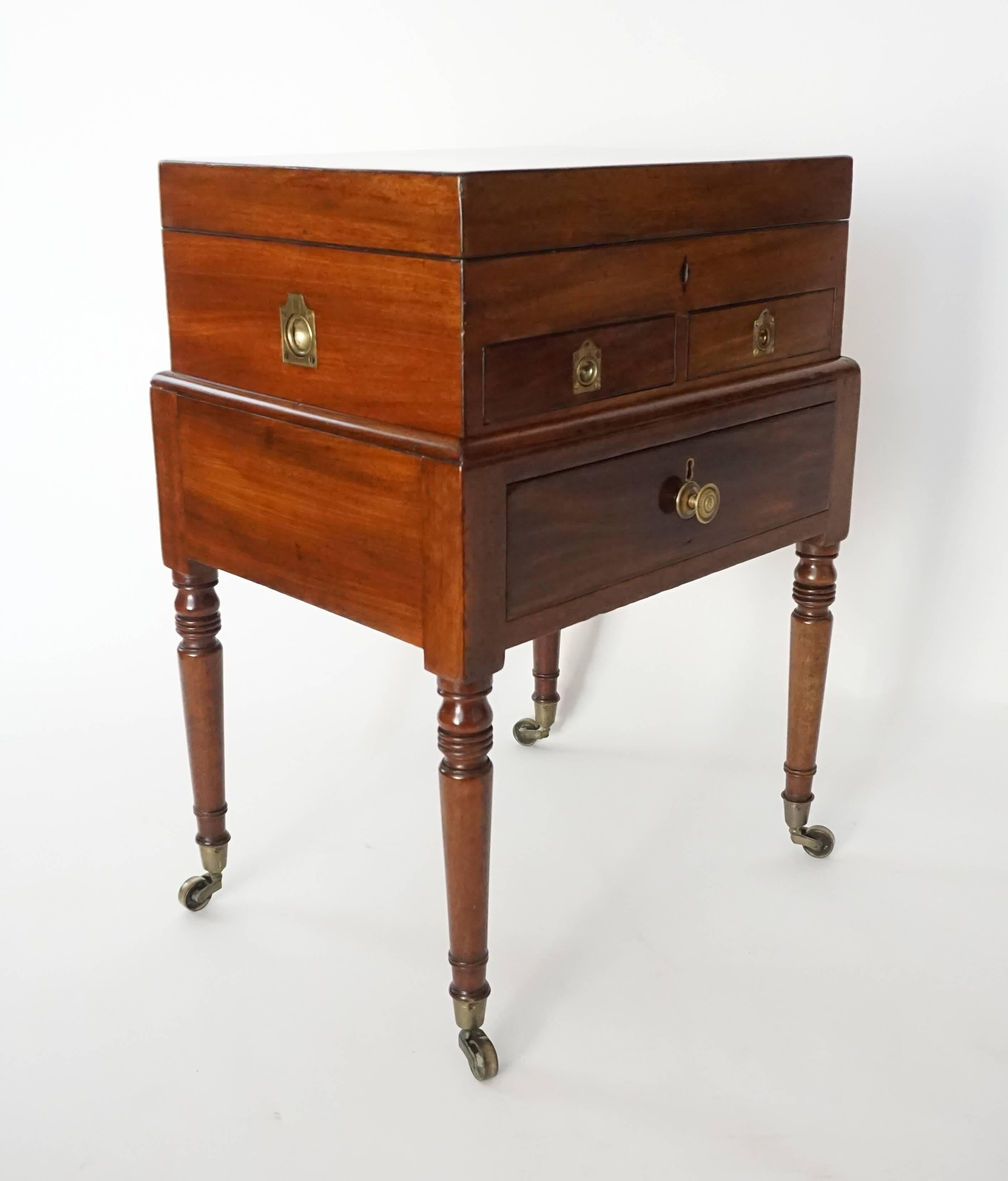 English Regency period mahogany British campaign chest or box on stand, circa 1820; the removable chest having hinged top revealing locking upper storage compartment above two internally locking lower drawers with divided compartments; the exterior