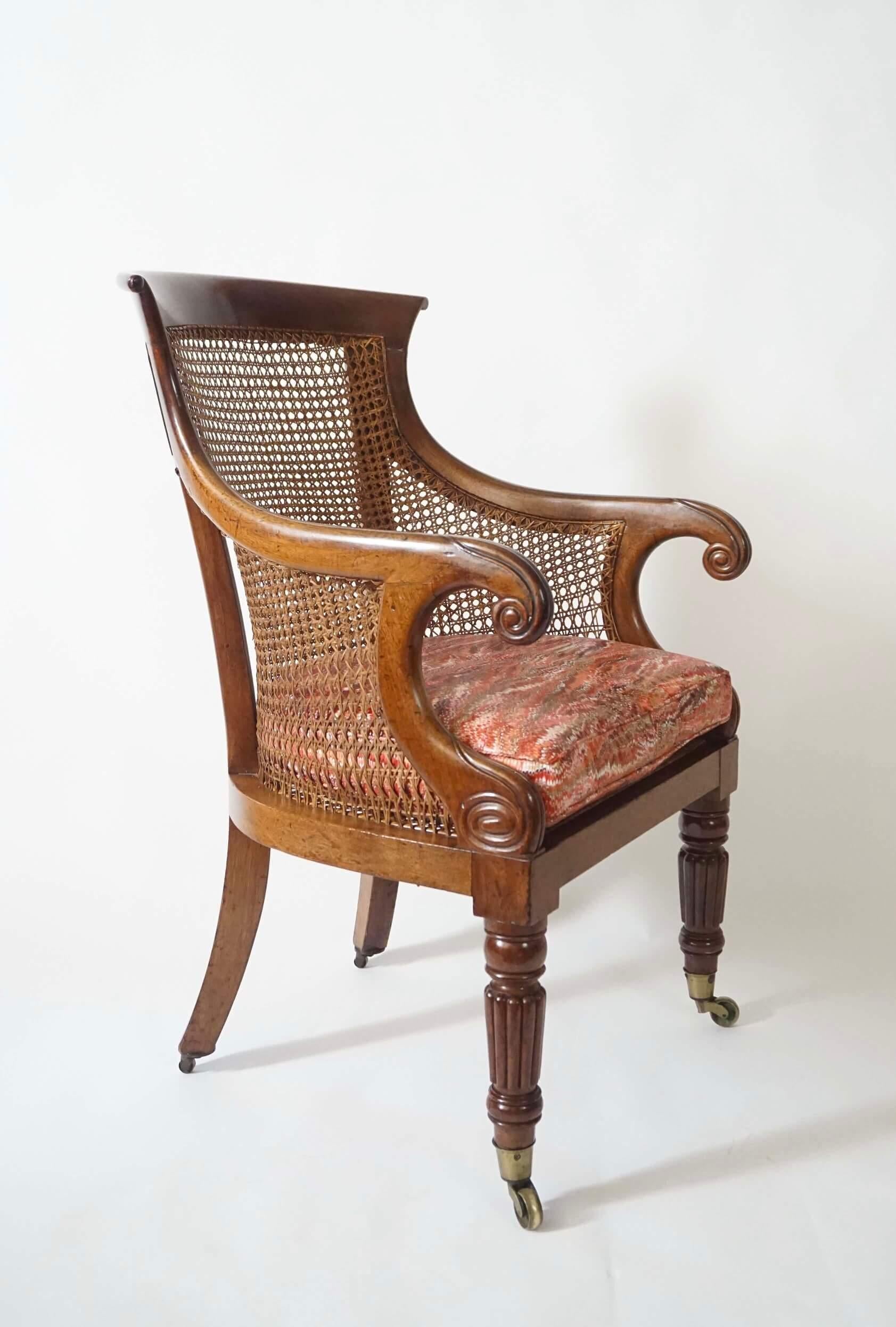 Ein eleganter um 1830 englischer Regency-Sessel oder Bergere aus massivem Mahagoni mit geformter Kammschiene und Schneckenarmen mit lotusgeschnitzten Endstücken und Volutenarmstützen mit kanonierter Rückenlehne, Seiten und Sitz mit losem Sitzkissen