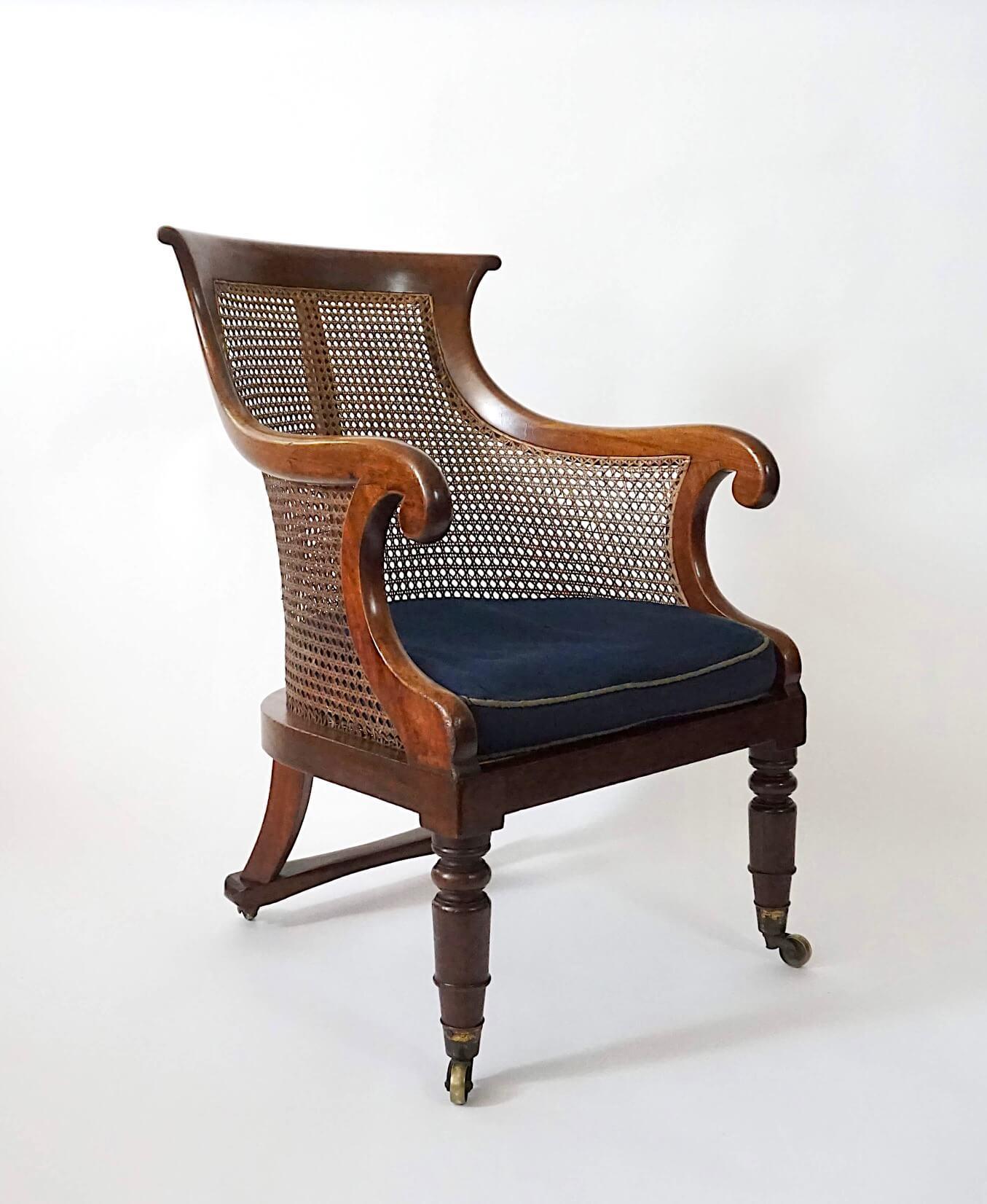 Un'insolita poltrona o bergere in stile reggenza inglese del 1830 circa, con struttura in mogano massiccio che presenta una linea di cresta sagomata e braccioli a voluta con schienale, fianchi e sedile a canne sciolte su gambe anteriori tornite e