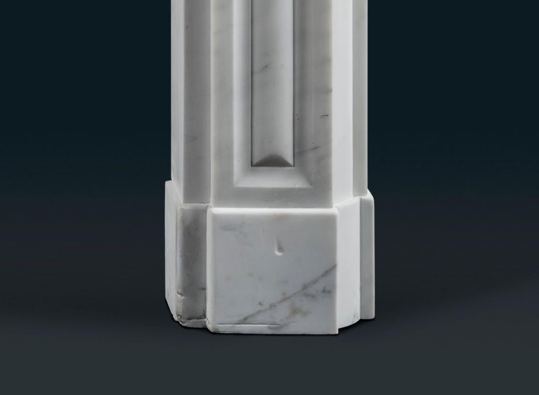 A late Regency period Carrara marble fireplace surround, the stepped shelf above panelled frieze with elegant shallow arch with applied foliate roundel to the centre, the jambs with equivalent cushion-mould panels, on block feet.

English,