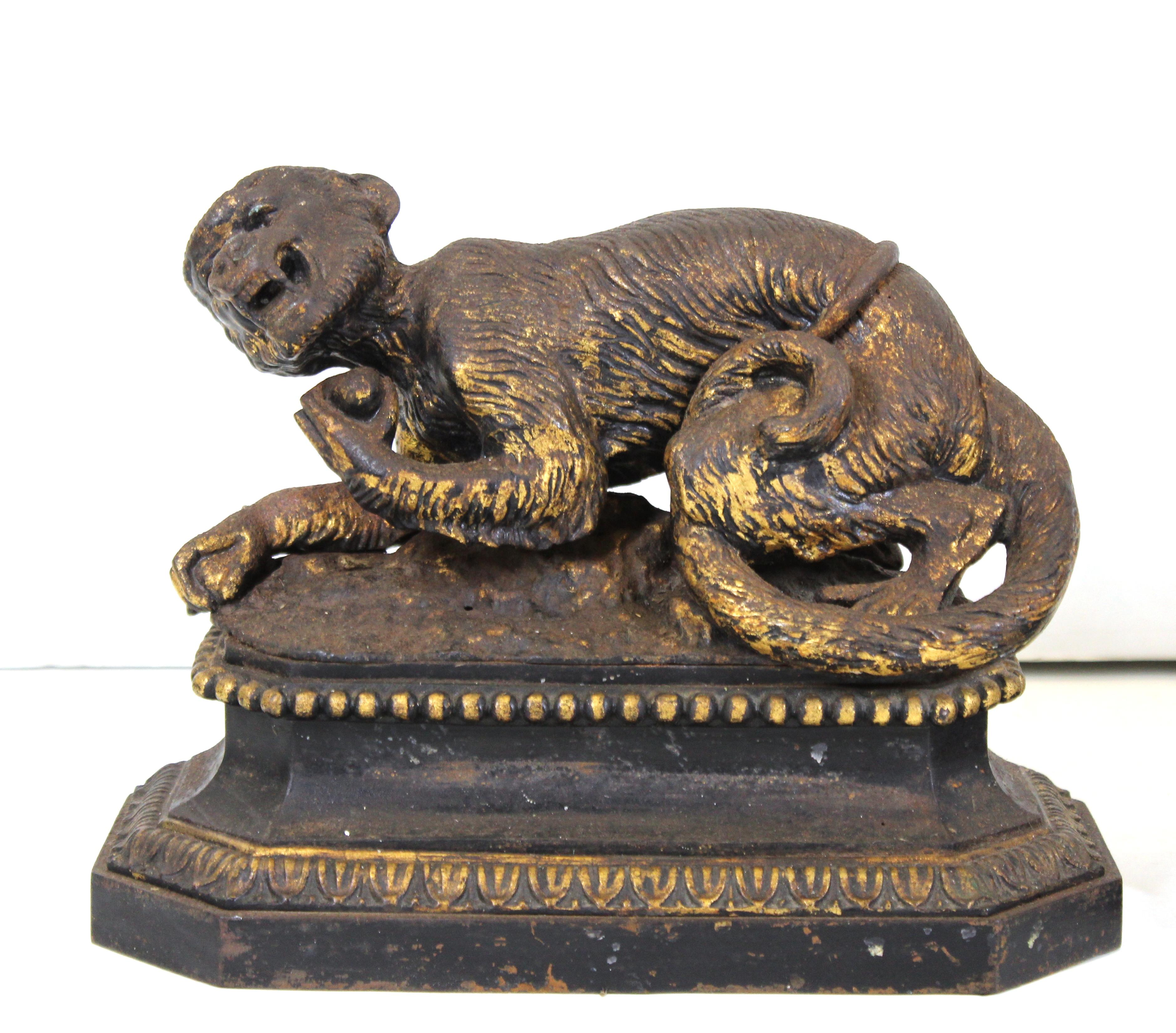 English Regency pair of black cast iron and partially gilt fireplace andiron chenets in the shape of monkeys holding fruit, atop decorative octagonal bases. The monkeys have expressive faces and appear to be tied up with rope around their back. Made