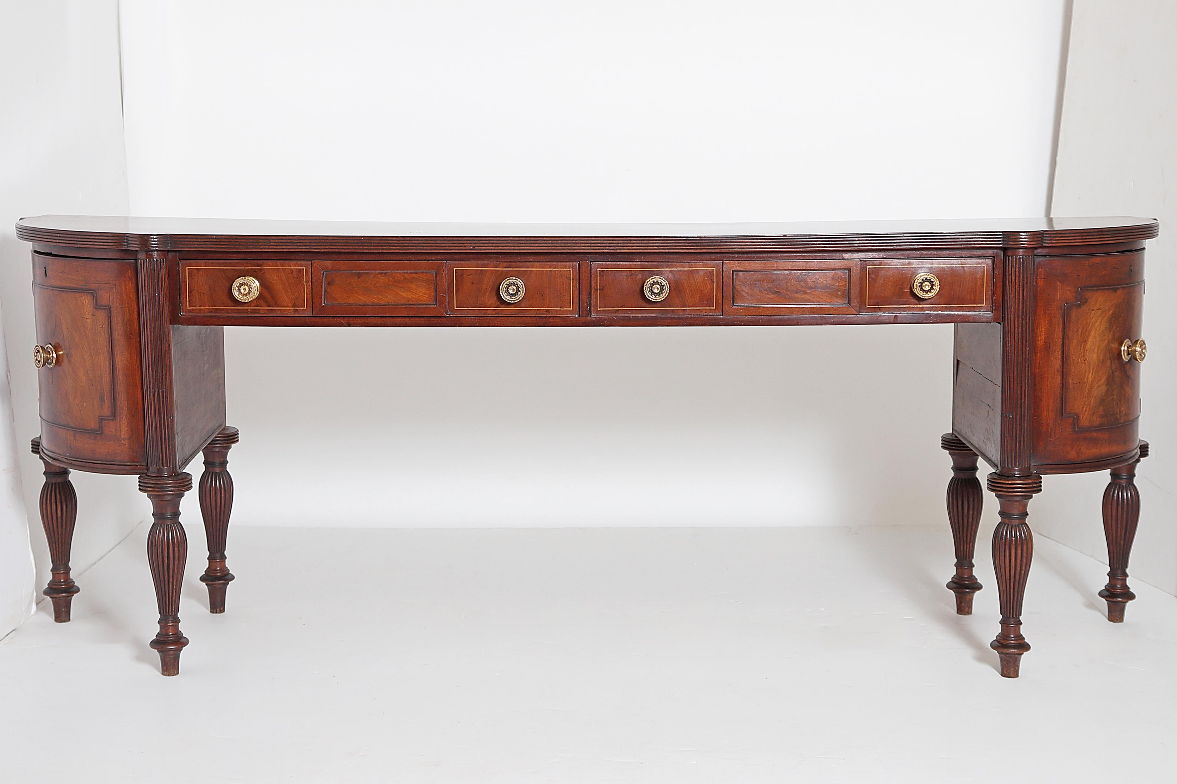 A circa 1810 English Regency sideboard of beautiful figured mahogany with two (2) long central drawers flanked by hinged (they swing out, see images) lead lined cellerets each partitioned for six (6) bottles, single board top with inlaid stringing,