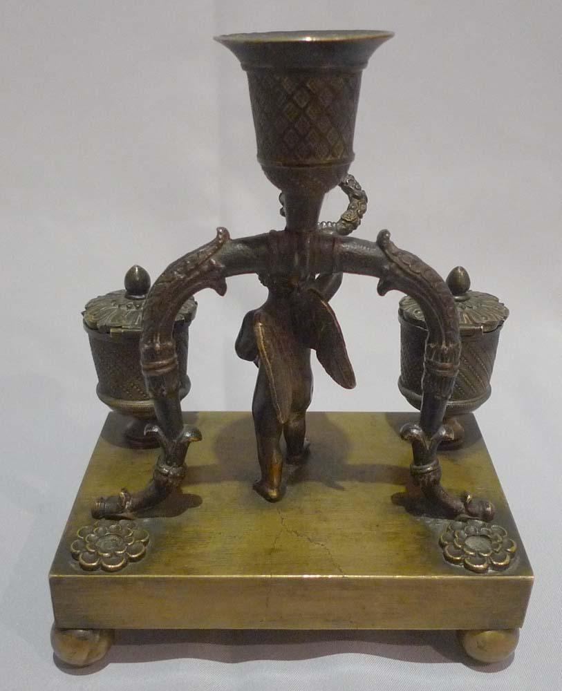 Antique English Regency figural inkwell with candle holder.
In finely cast and original patinated bronze.
Set on ball feet the rectangular base has a figure of Cupid holding up a wreath between very well cast ink pot and sand pot with bodies