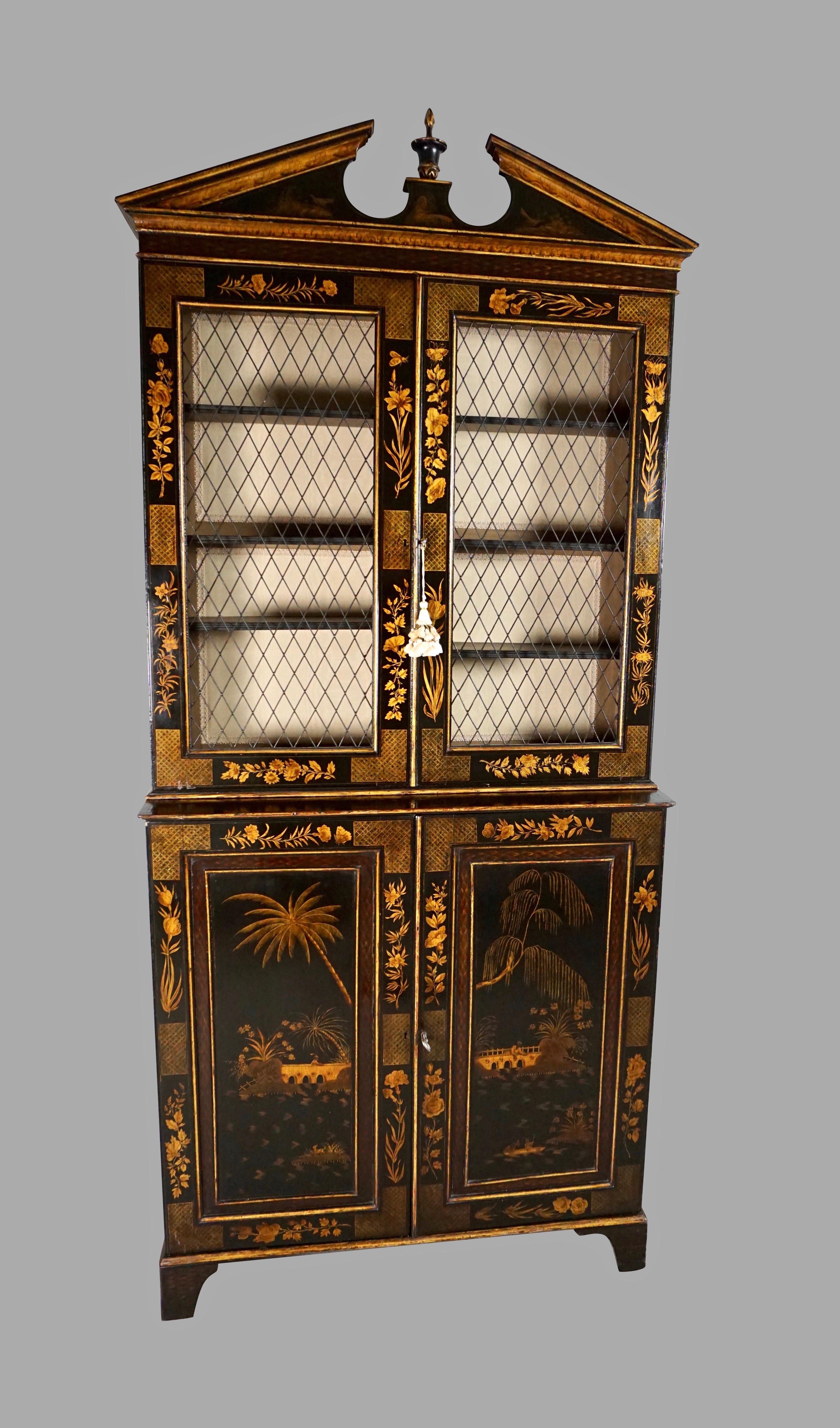 An elegantly proportioned English Regency period black and gold chinoiserie bookcase cabinet, the broken pediment cornice decorated with finely drawn birds centered by a vasiform finial, the lined upper stage with a painted interior and adjustable