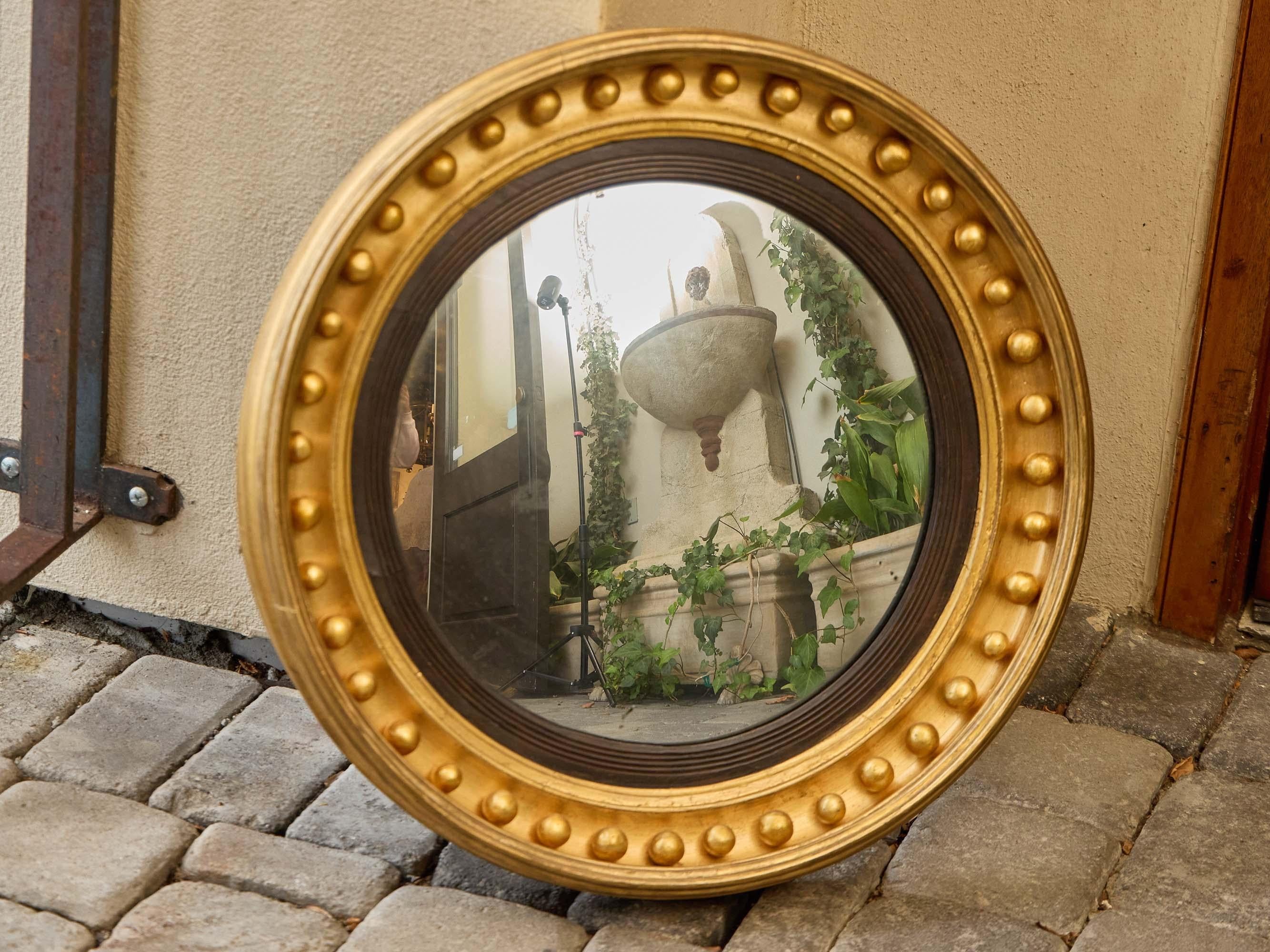 A striking 19th-century English convex mirror in the Regency style, featuring a circular giltwood frame embellished with a prominent row of evenly spaced spherical bosses. The inner border is encircled with ebonized reeded detailing, creating a bold