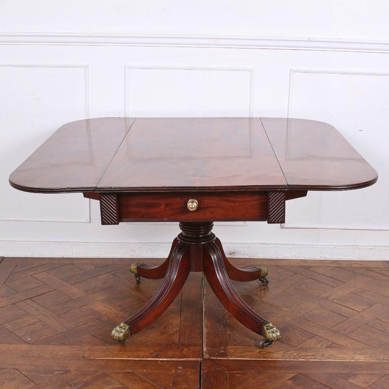 An English Regency drop-leaf breakfast table, the top fitted with a single drawer and raised up on a turned pedestal with out-swept sabre legs terminating in original brass castors. 

23.5 inches Wide (Closed) x 40 inches Wide (Open) x 48 inches