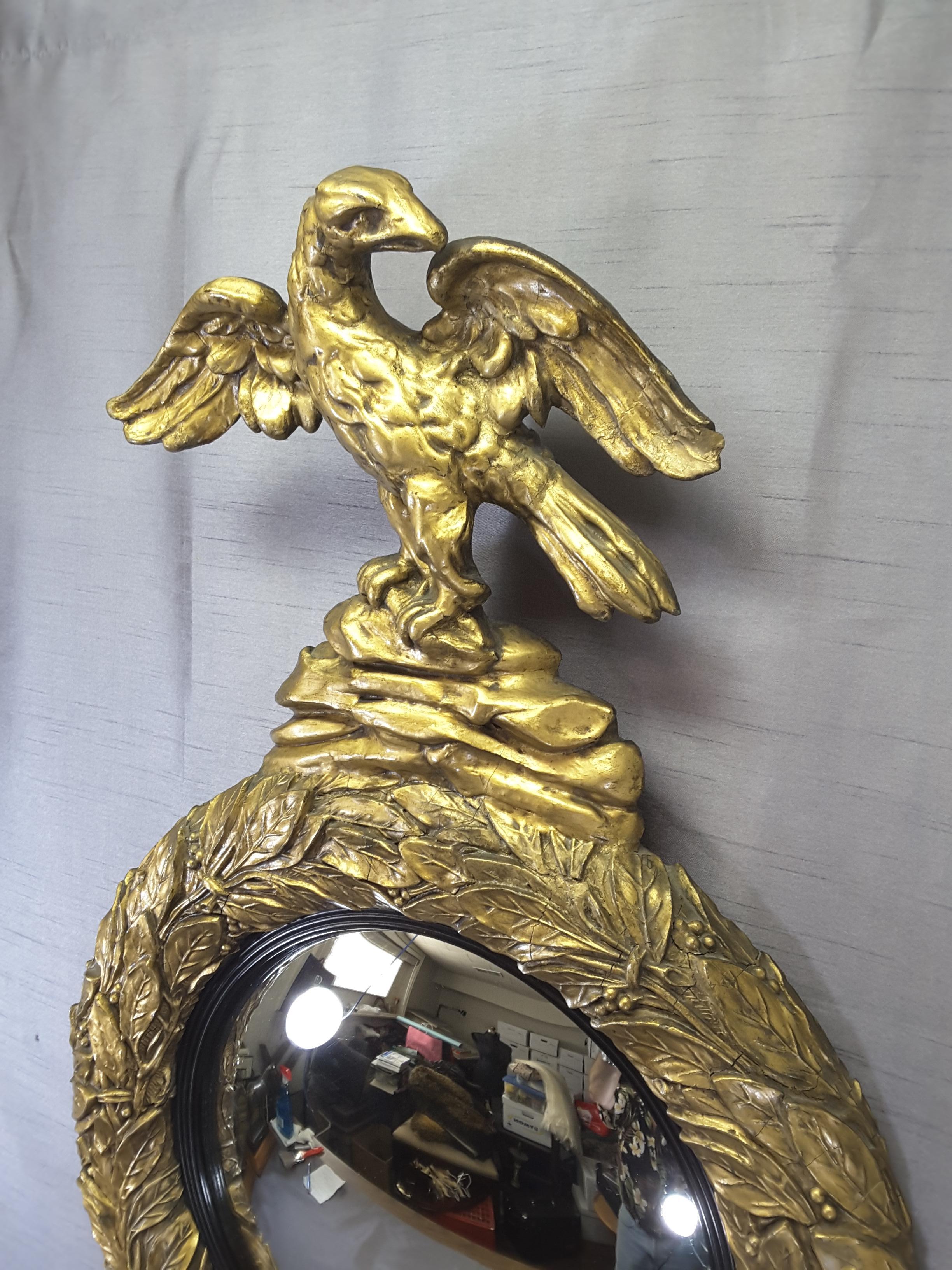 English Regency eagle gilt convex bullseye mirror, berries and leaf pattern and black ebonised mirror trim. Extended wings eagle standing on rock bluff on the top of the mirror, slight right wing tip loss to the wing as per photo, the mirror is in
