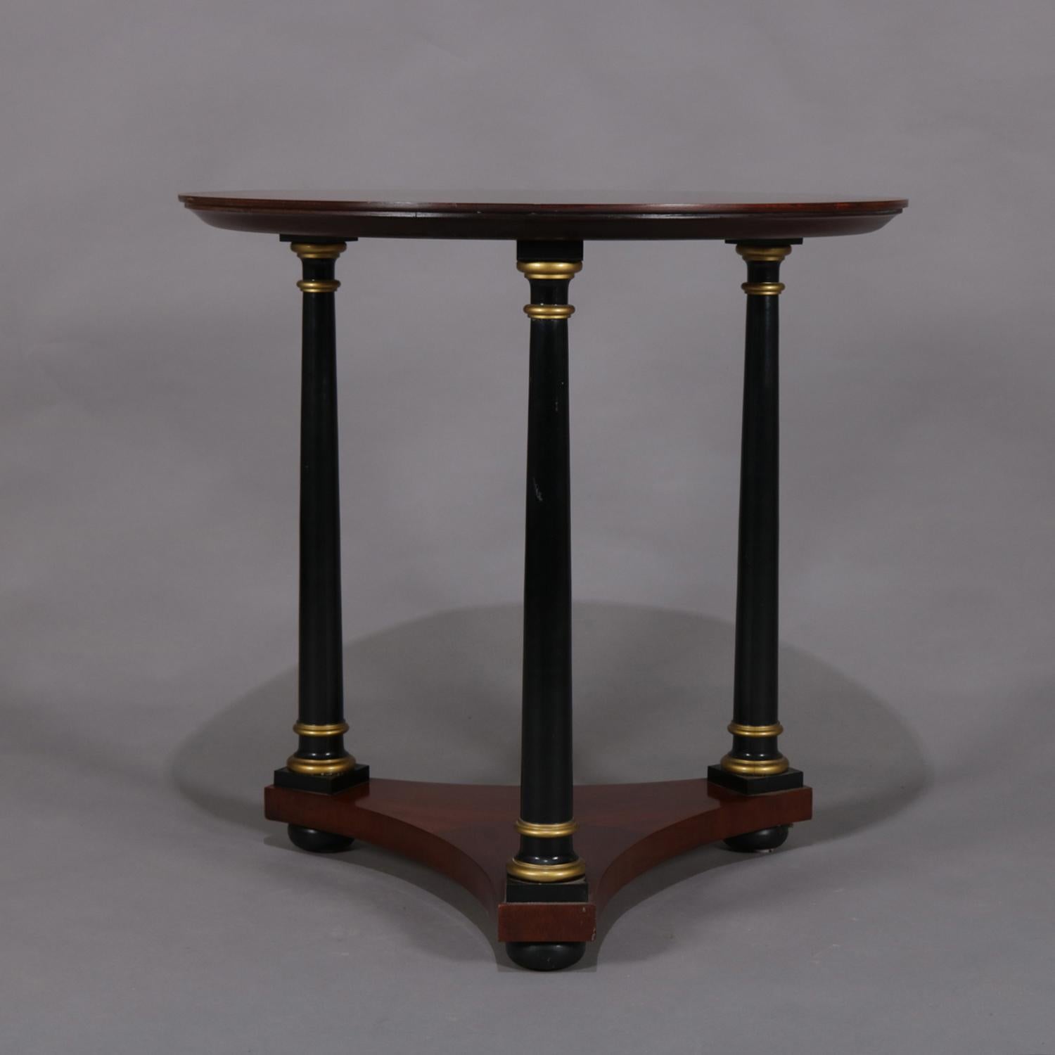 English Regency style centre table features mahogany construction with round and bookmatched top supported by three ebonized Corinthian column-form supports having gilt highlights and seated on triangular plinth raised on ebonized ball feet, 20th