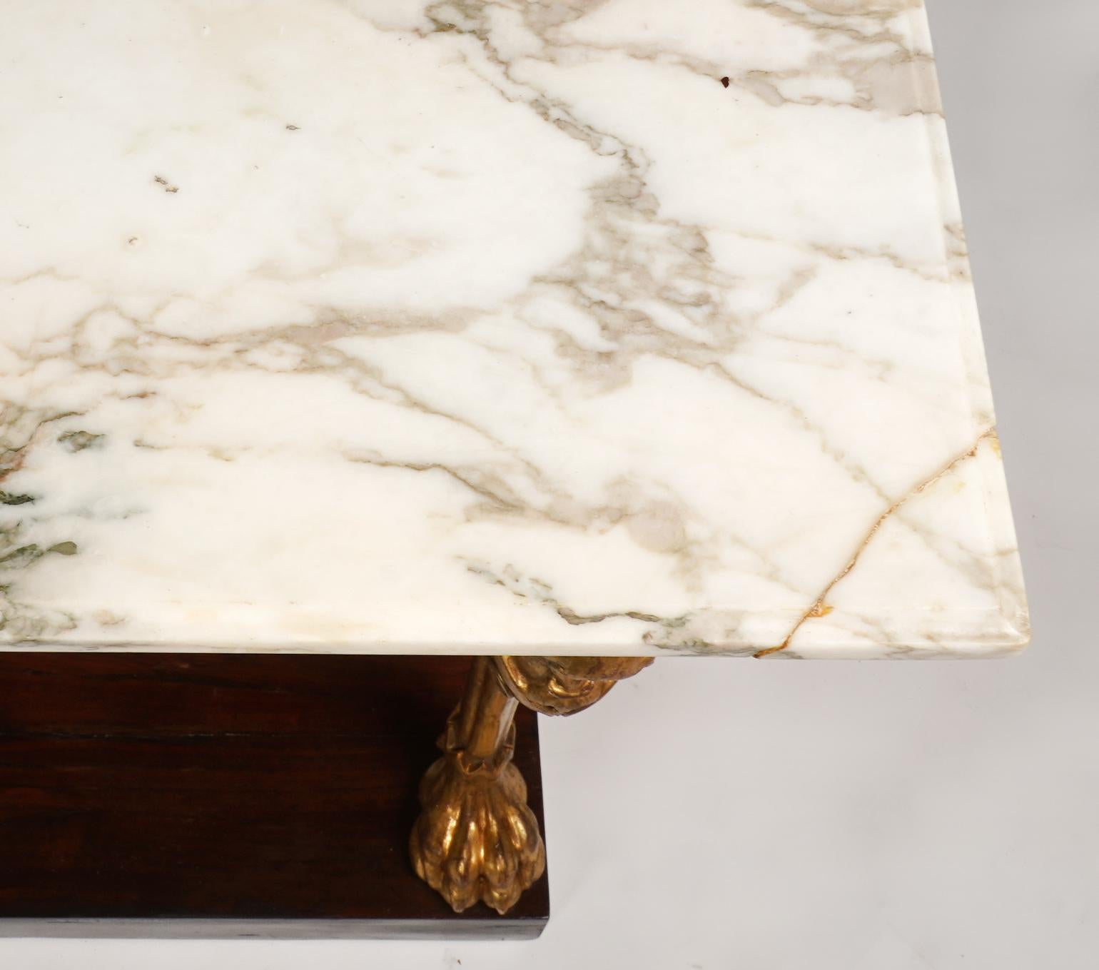 This fine Regency console table dating to around 1820 features a marble top above a frieze with gilt bronze star mounts supported by two Egyptian Revival styled carved giltwood Lion legs with heads and naturally shaped legs and paws standing on an