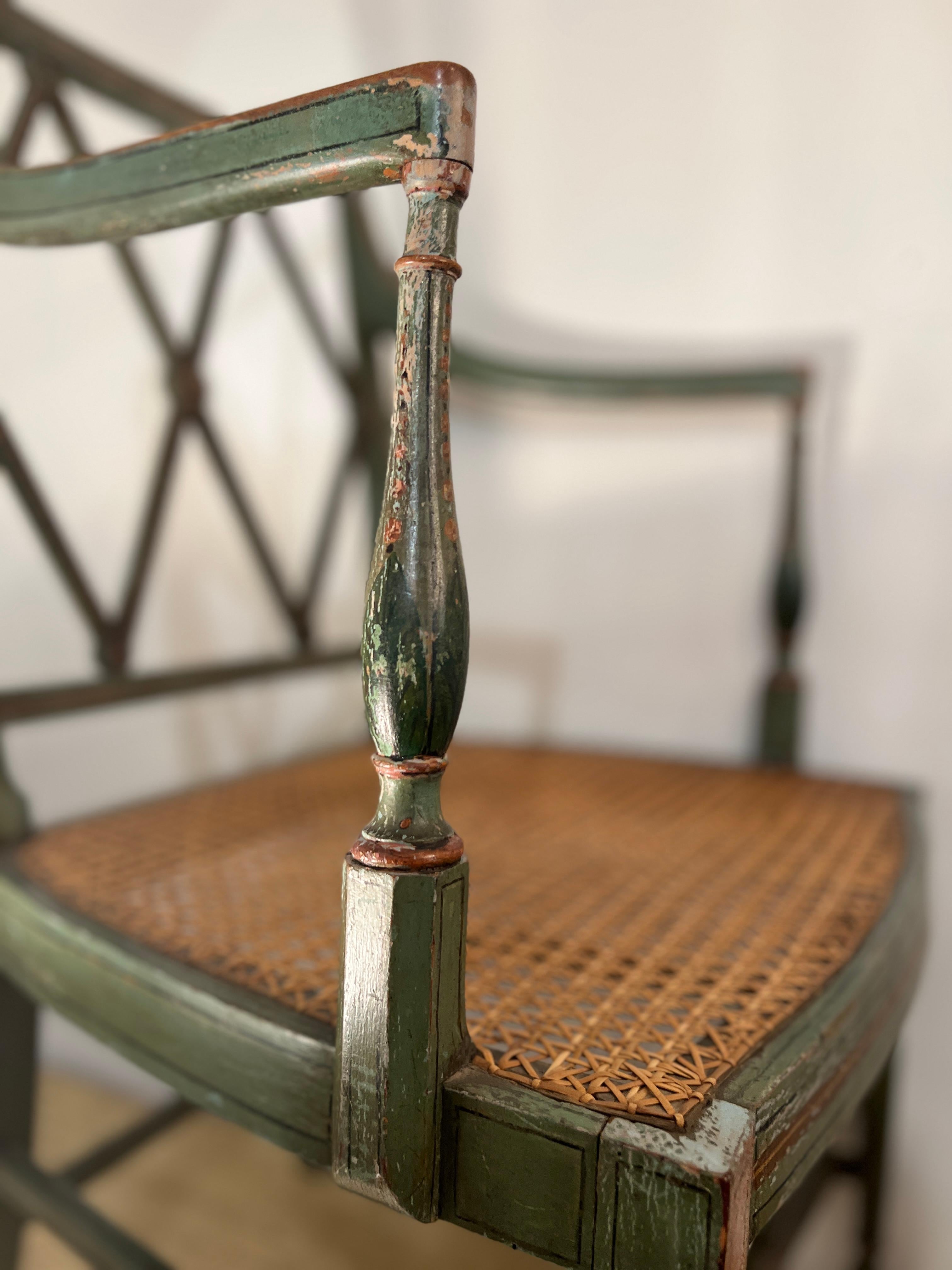 Original paint in a lovely green tone with hand-painted floral details. High arms, an diamond design back and a caned seat.