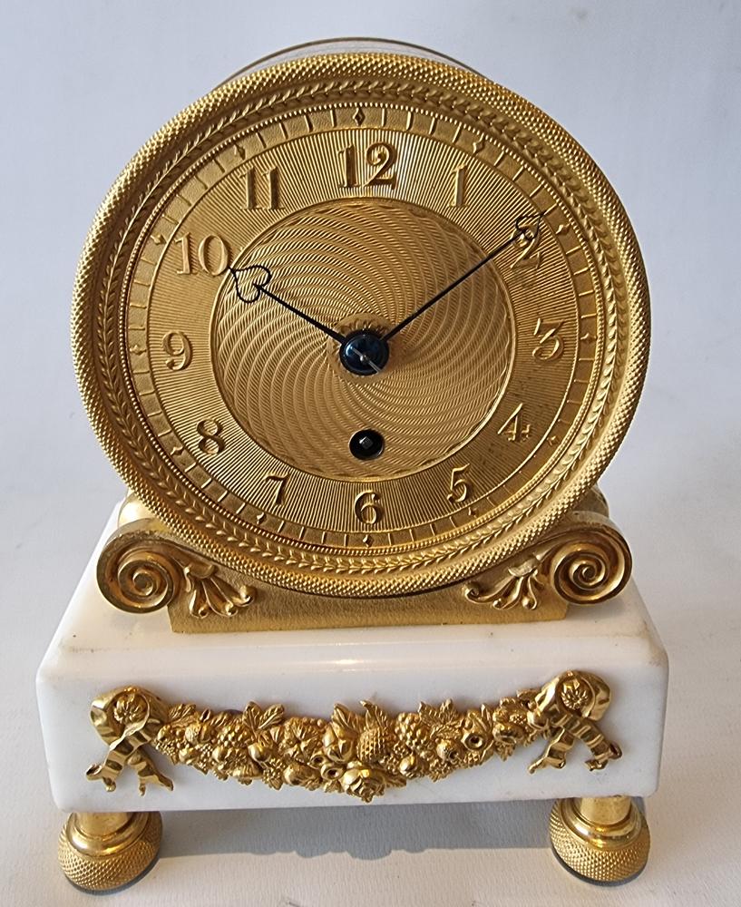 English Regency ormolu and white marble drum mantel clock. Typical drum shaped clock, set on four elaborate ormolu toupee feet. The white marble has an applied ormolu mount of flowers and fruit to the front. The ormolu drum case sits upon ormolu